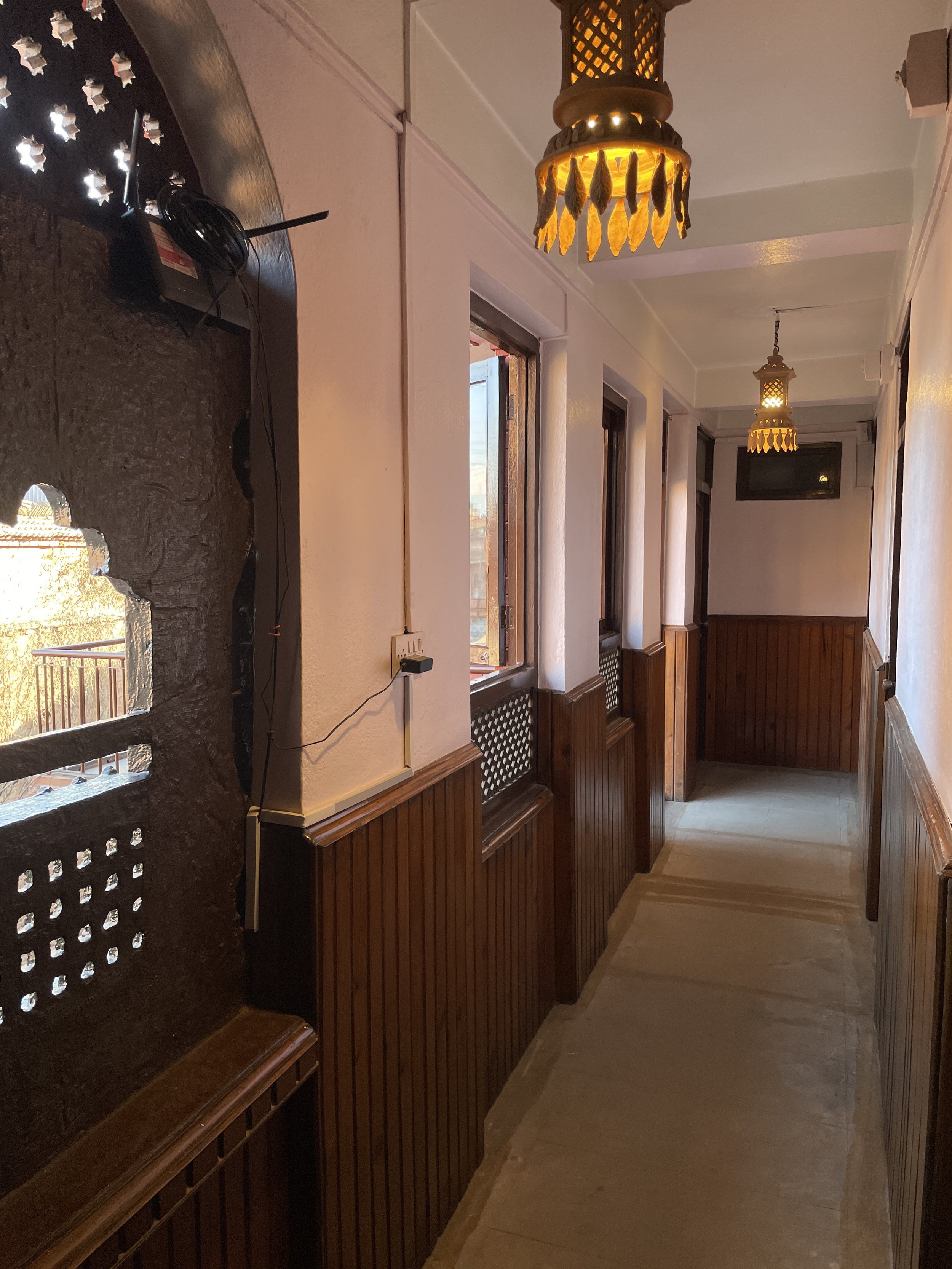 Interior hallway of Rato Ghar Boutique Hotel in Bhaktapur with traditional wood paneling and warm lantern lighting.