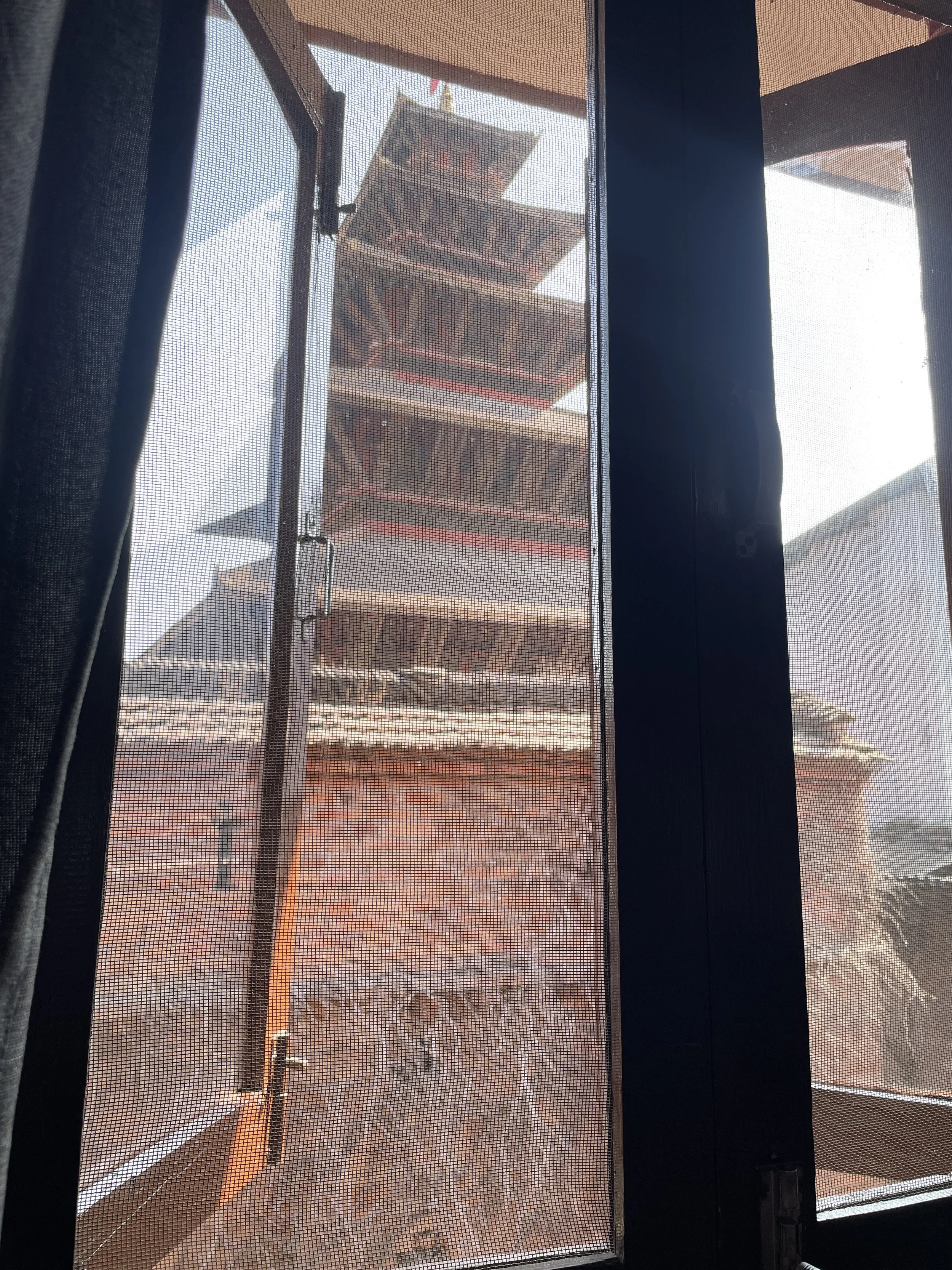 View of a multi-tiered pagoda seen through a window with a screen, showing the pagoda's curved eaves and brick base.