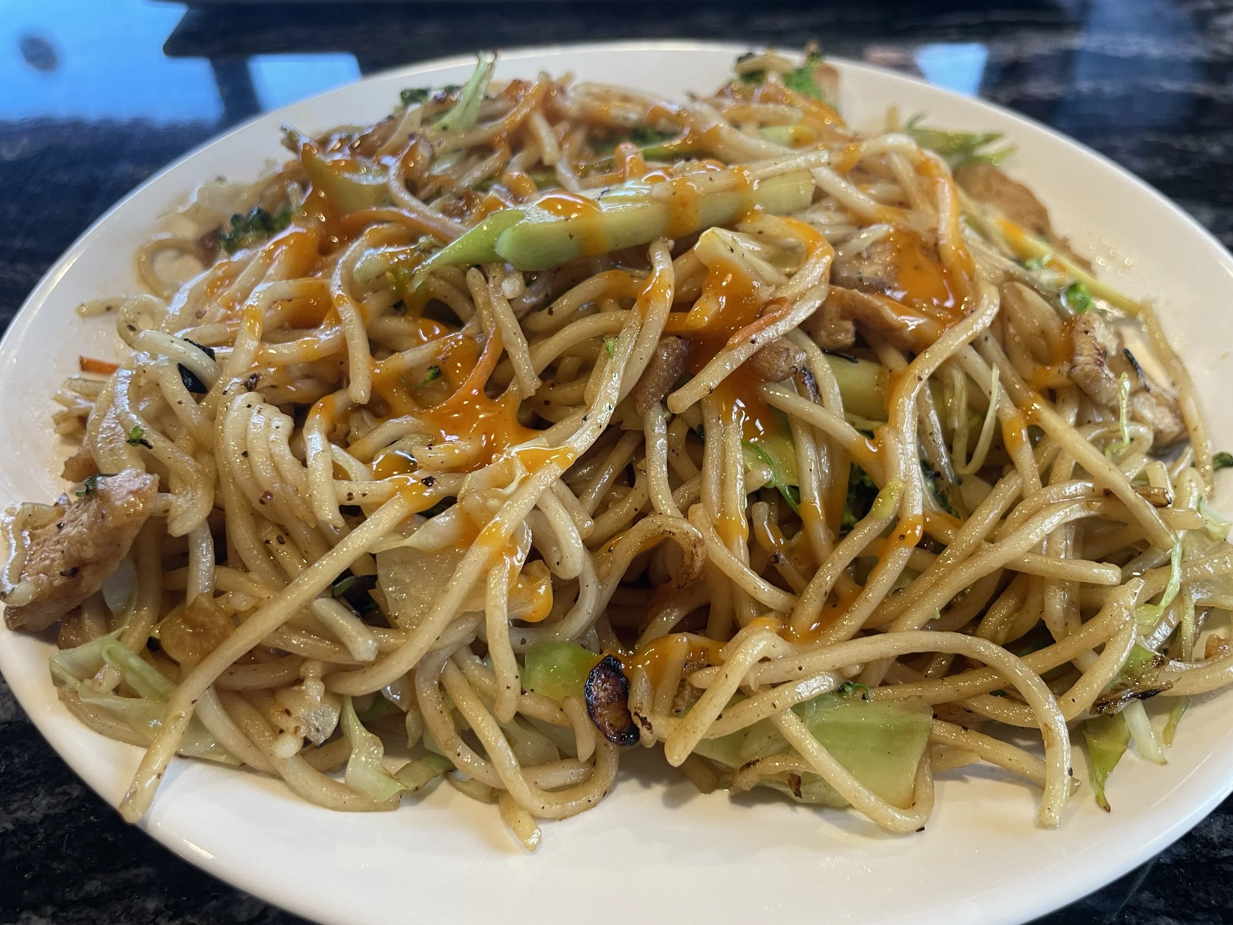A plate of stir-fried noodles with broccoli and chicken, drizzled with sauce.