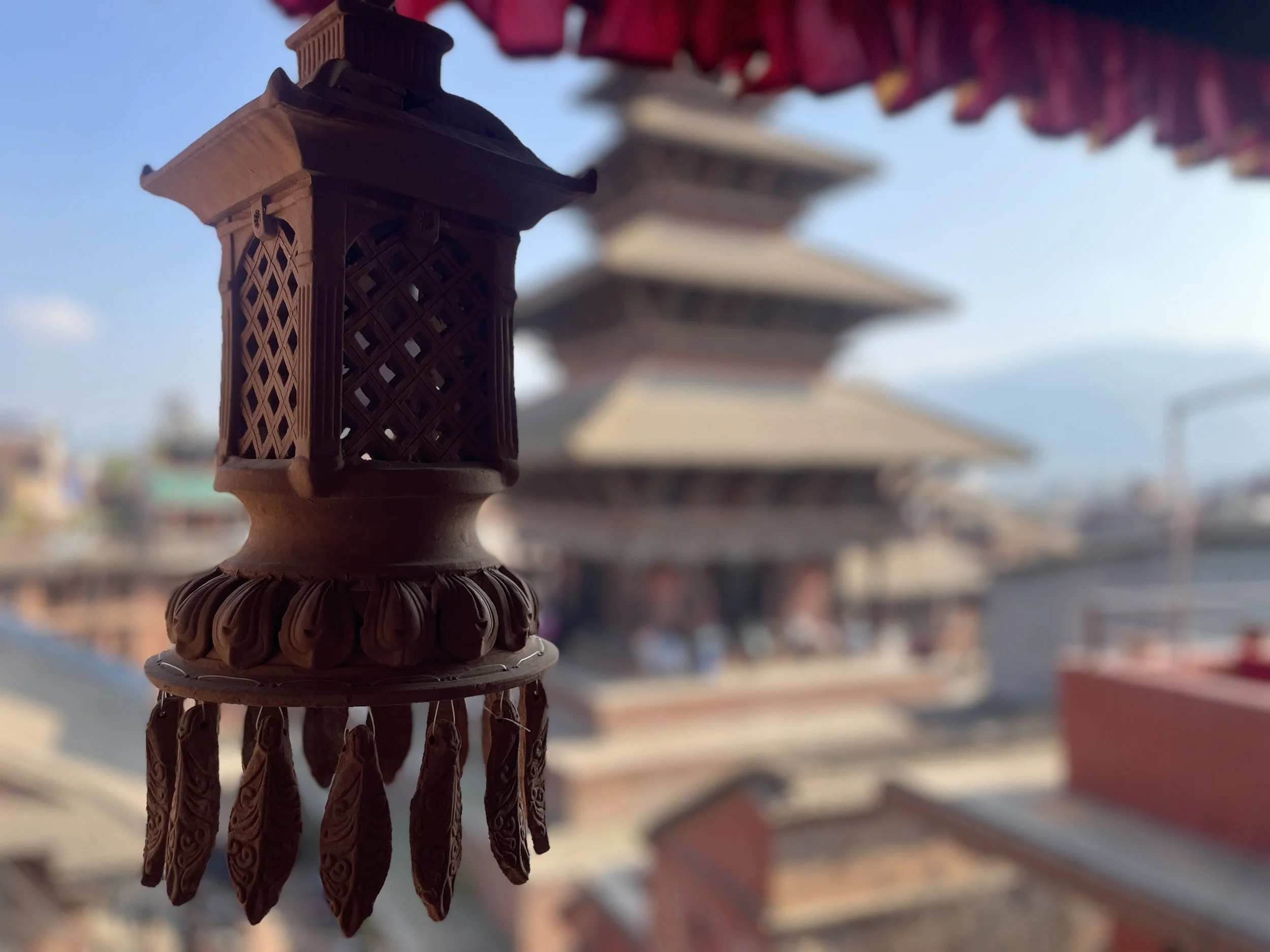 Close-up of a traditional pottery lantern with a temple in the background, under a clear blue sky.