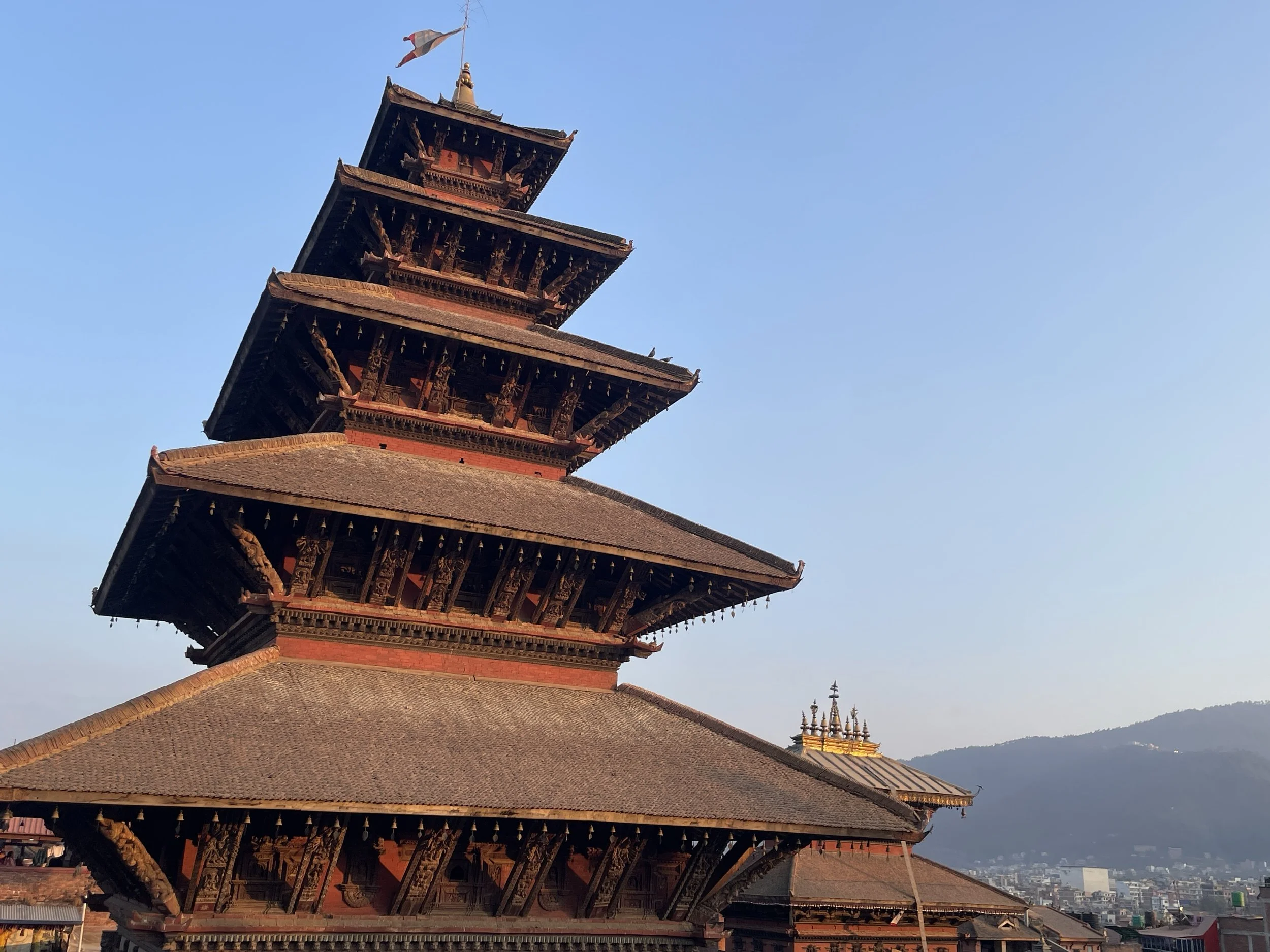 Traditional five-tiered pagoda in a city setting with mountains in the background during sunset.