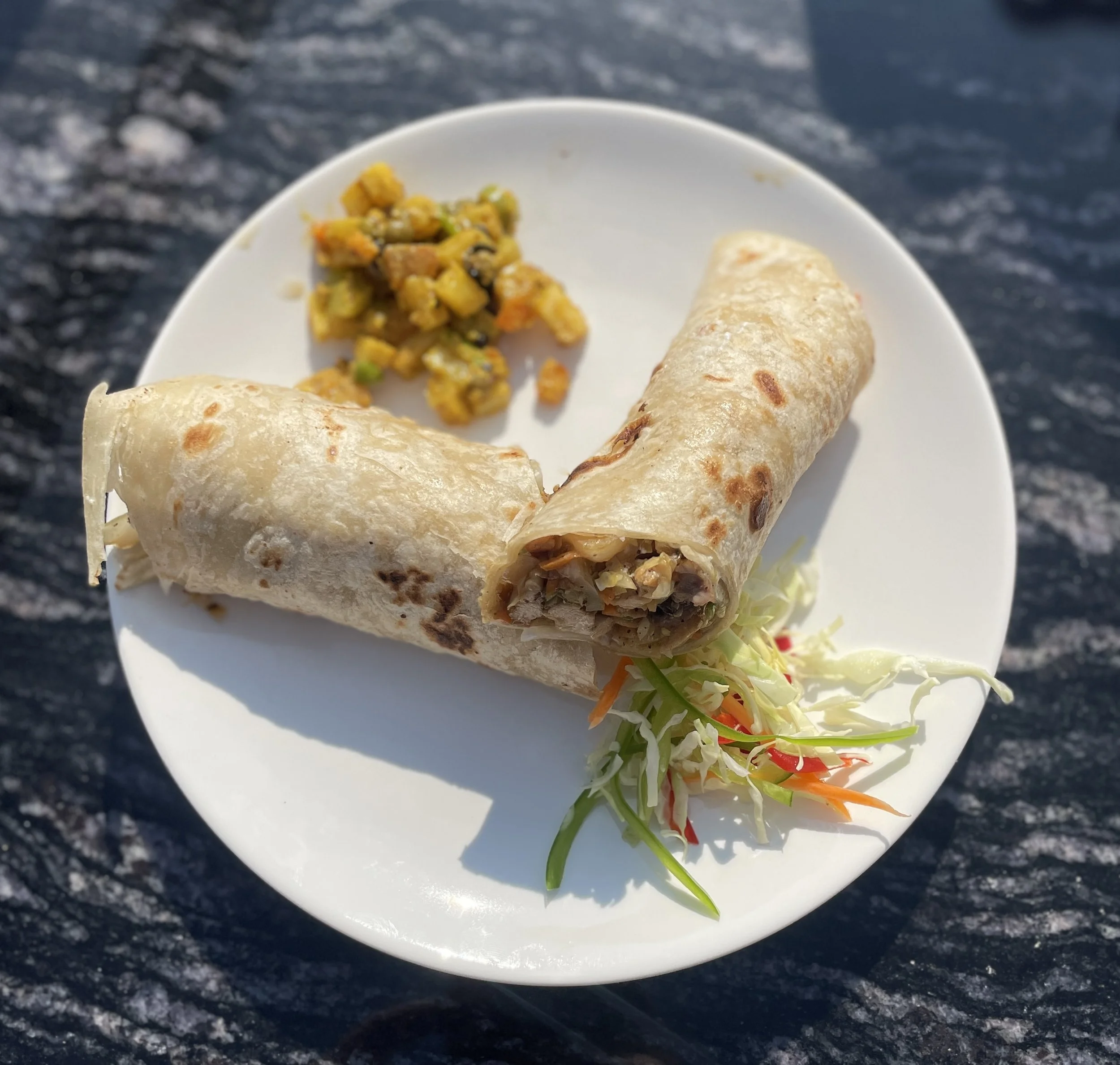Plate with a rolled wrap, and shredded cabbage cole slaw, and a serving of radish pickle on a white plate outside.