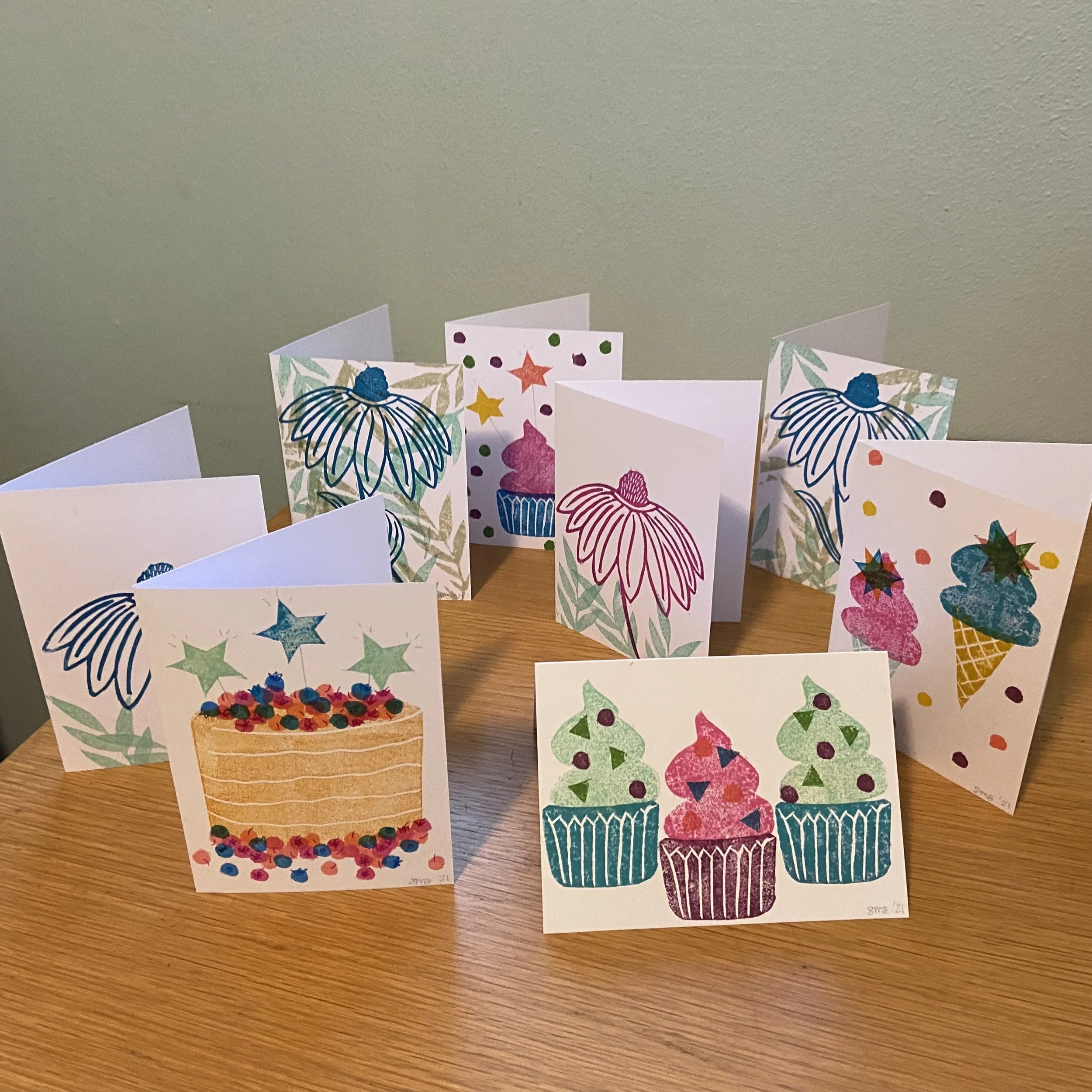 Collection of colorful handmade birthday cards with cupcake and party-themed illustrations on a wooden table.