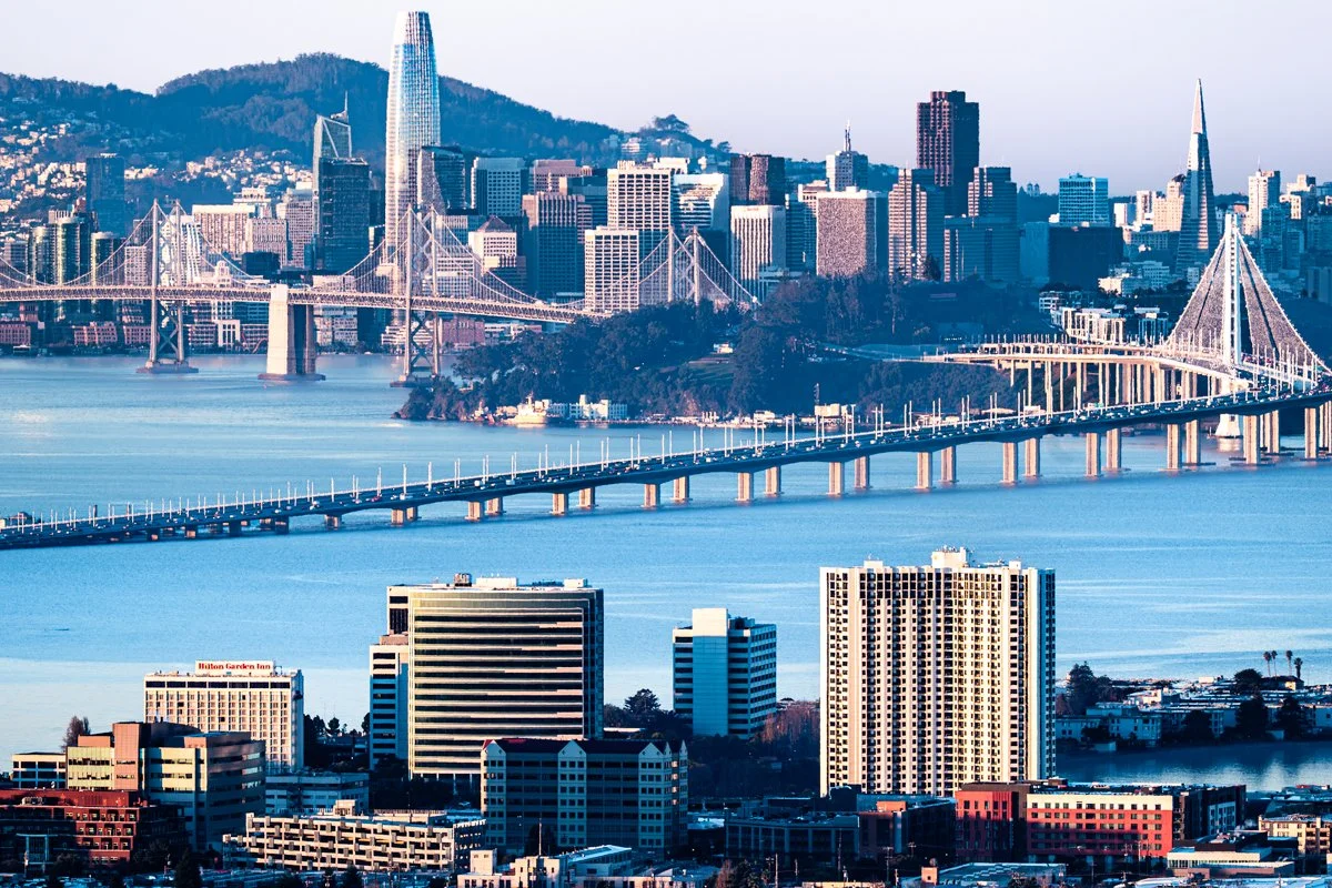 Skyline of San Francisco with the Bay Bridge in the foreground and various skyscrapers in the background, including the Salesforce Tower and Transamerica Pyramid.