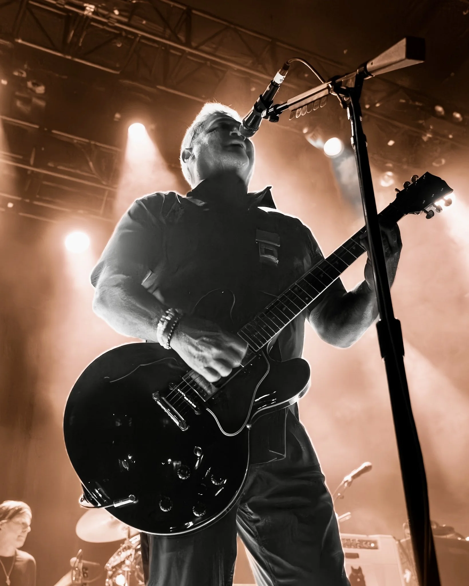 A person playing electric guitar and singing into a microphone on stage with bright lights, viewed from a low angle.