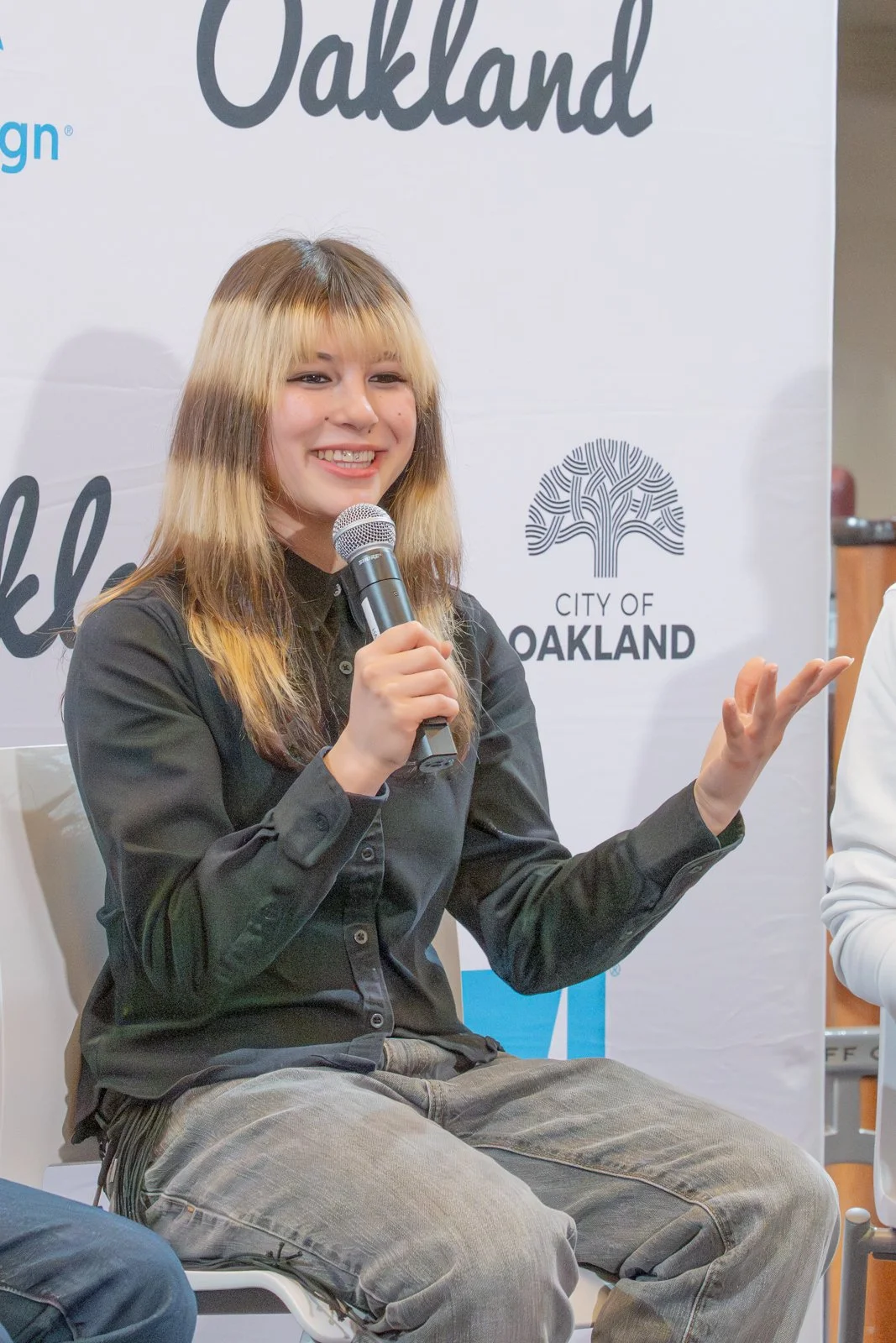 Coastal landscape with green grassy hills, a turquoise ocean, rocky cliffs, and a wooden fence in the foreground under a partly cloudy sky.