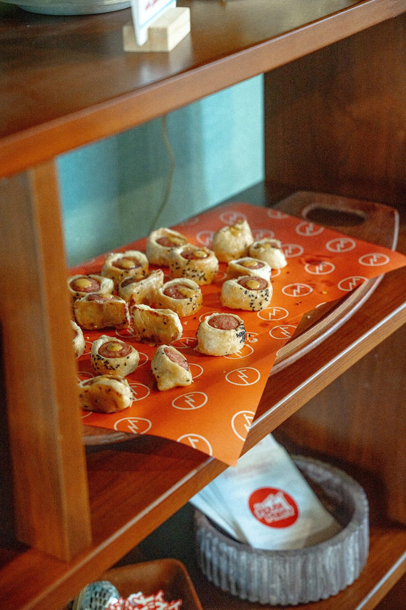 Sushi rolls with raw fish and rice on orange paper inside a wooden display case.