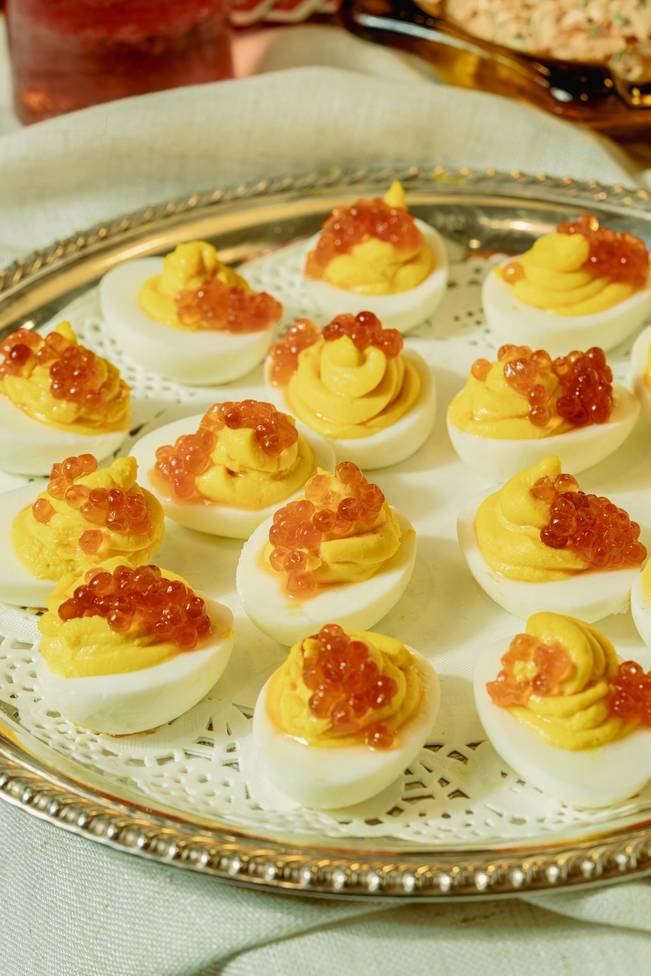 Deviled eggs topped with orange fish roe on a silver platter.