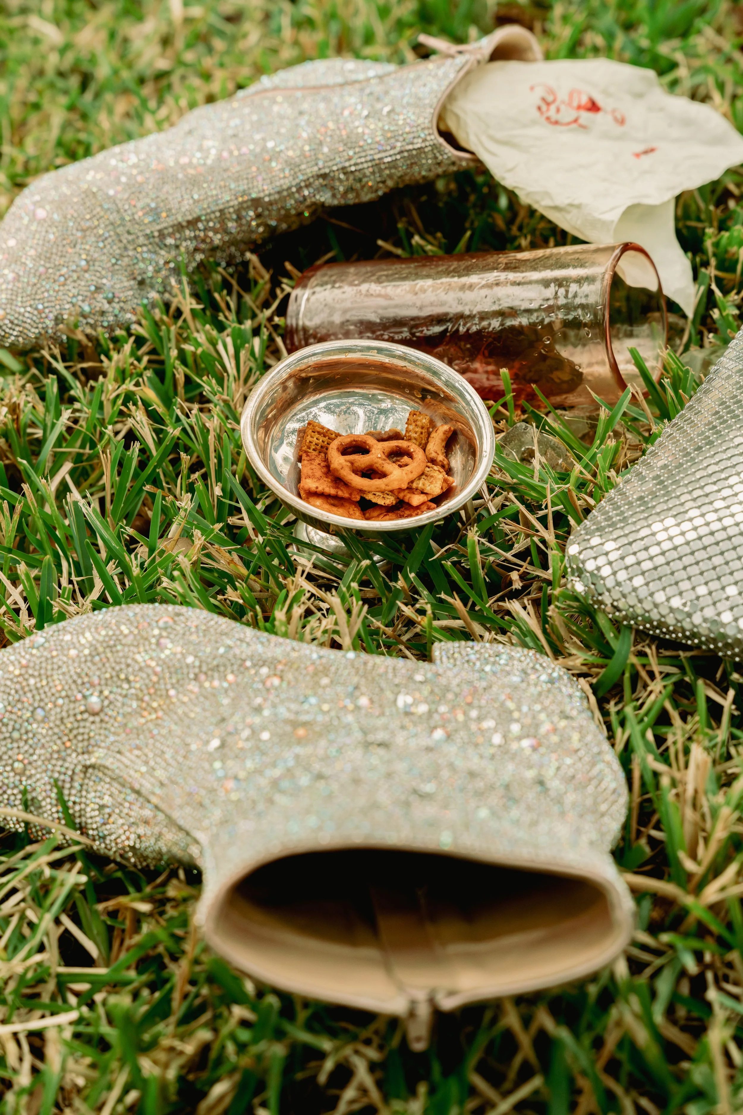 Glitter ankle boots on grass with spilt chex mix and cocktail glass