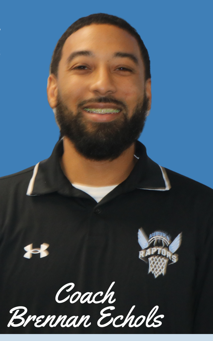 A man with dark curly hair, glasses, and a nose ring, wearing a dark sweater, sitting in a room with a neutral background and a plant in the background.