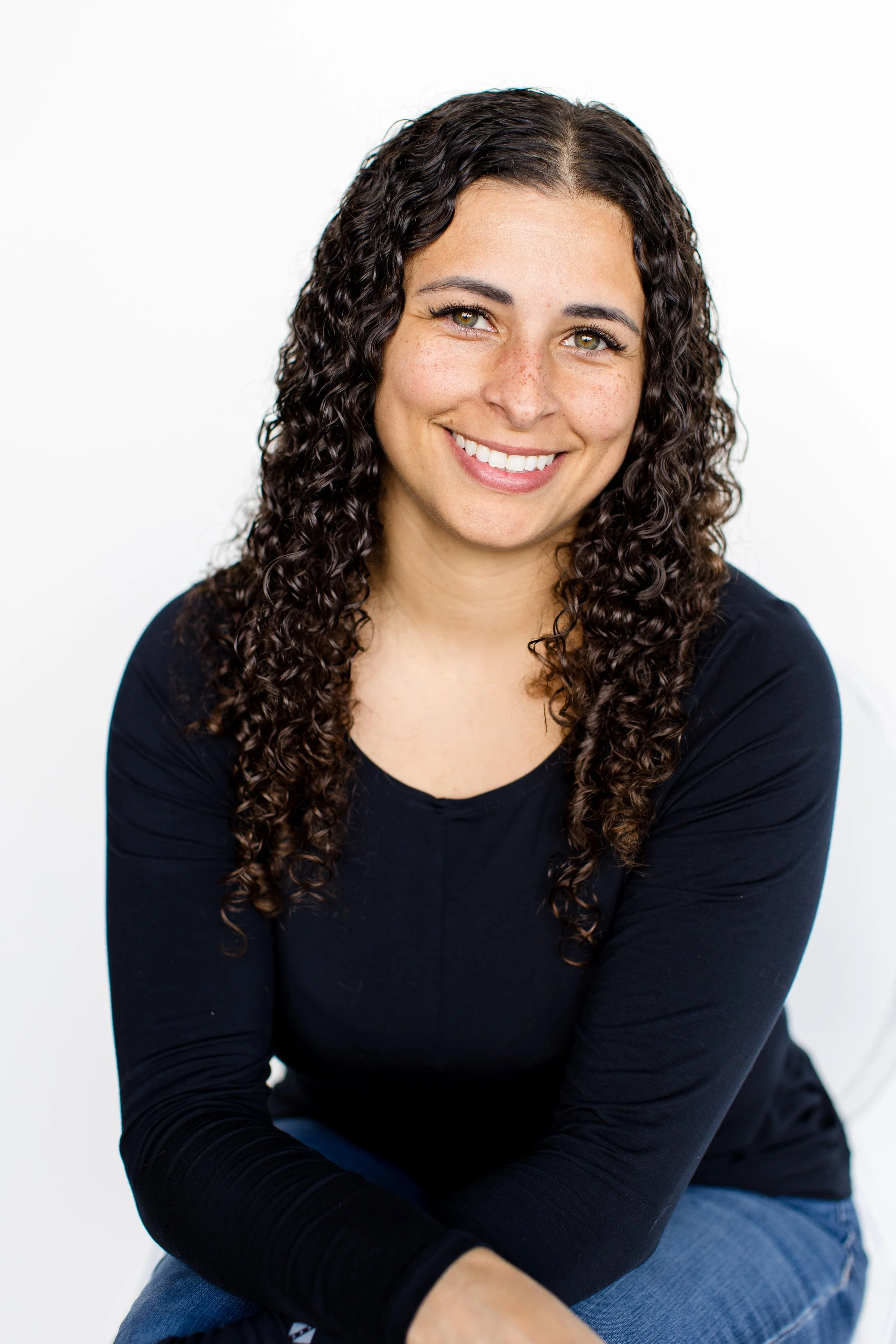 Portrait of a woman with long, curly dark hair, smiling, against a white background.