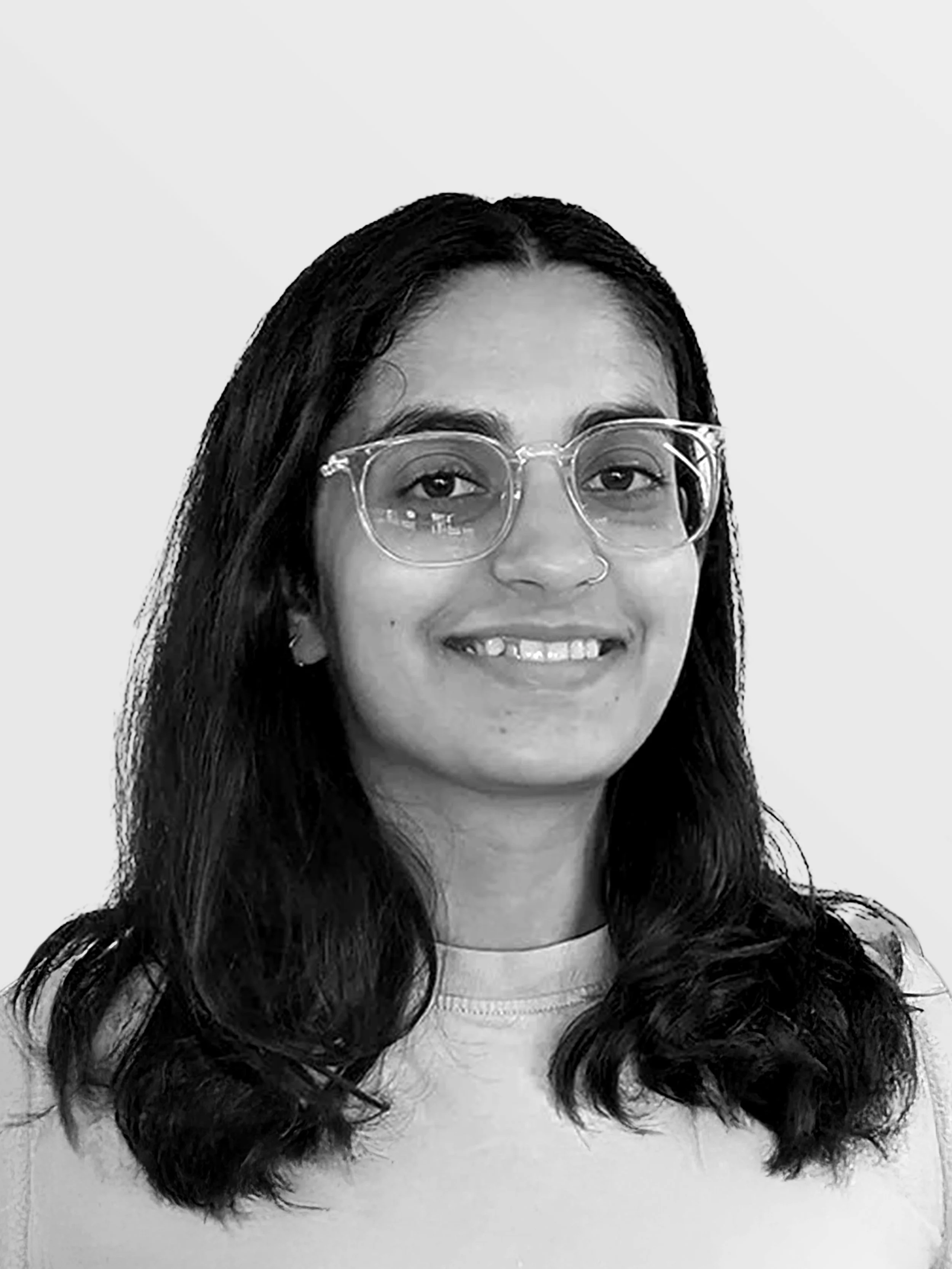 Black and white photo of a woman with long dark hair wearing large clear glasses and a light-colored shirt, smiling at the camera.