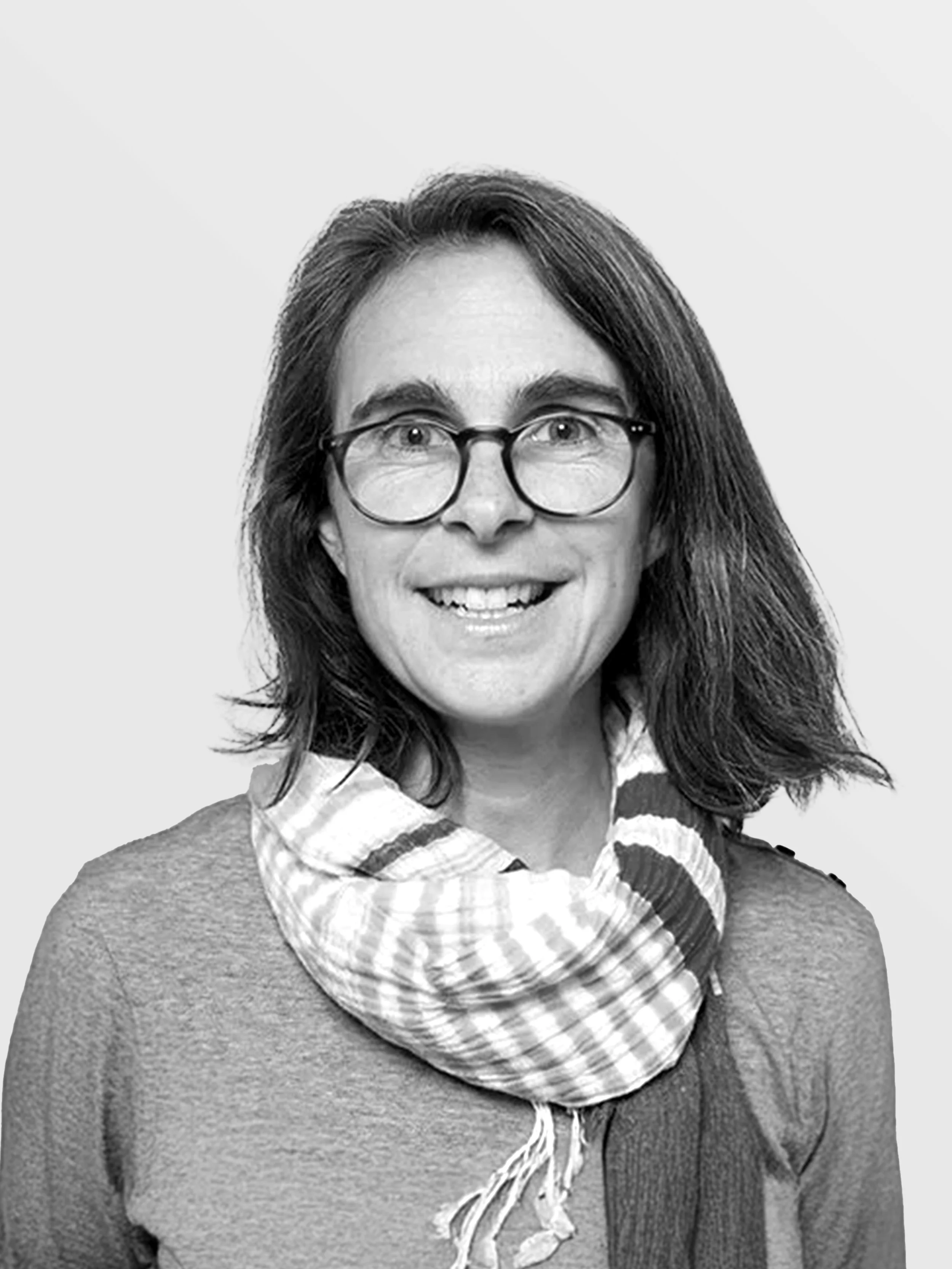 Black and white portrait of a smiling woman with shoulder-length hair, glasses, a scarf, and a sweater, against a plain background.
