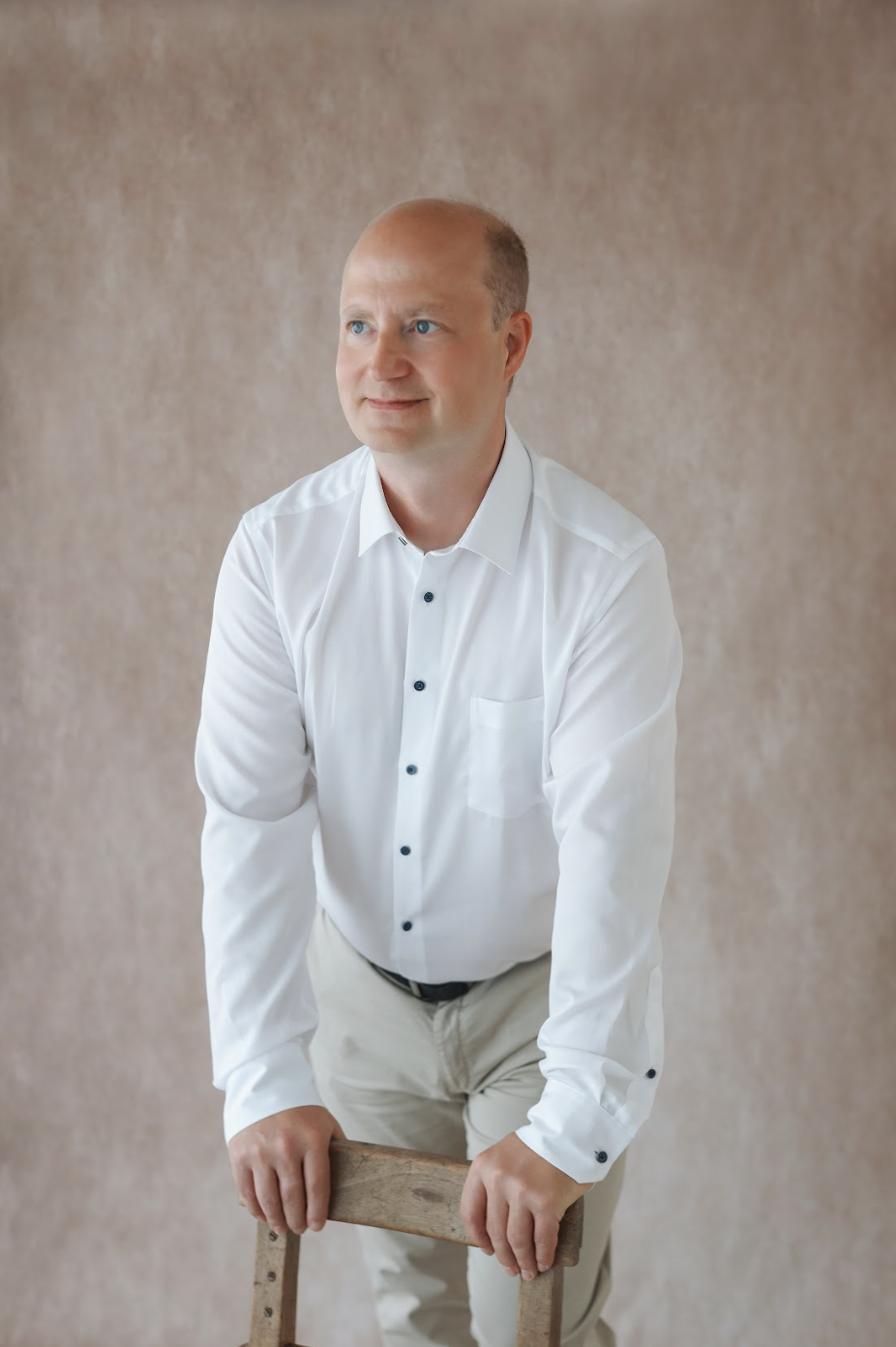 Ein Mann in weißen Hemd und cremefarbenen Hosen lehnt auf einem Stuhl.