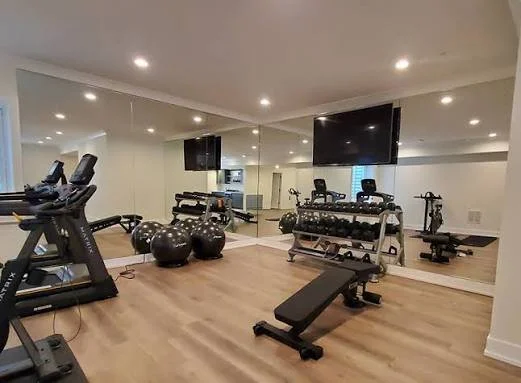 Home gym with treadmills, exercise balls, free weights, a flat bench, and a large mirror on the wall.