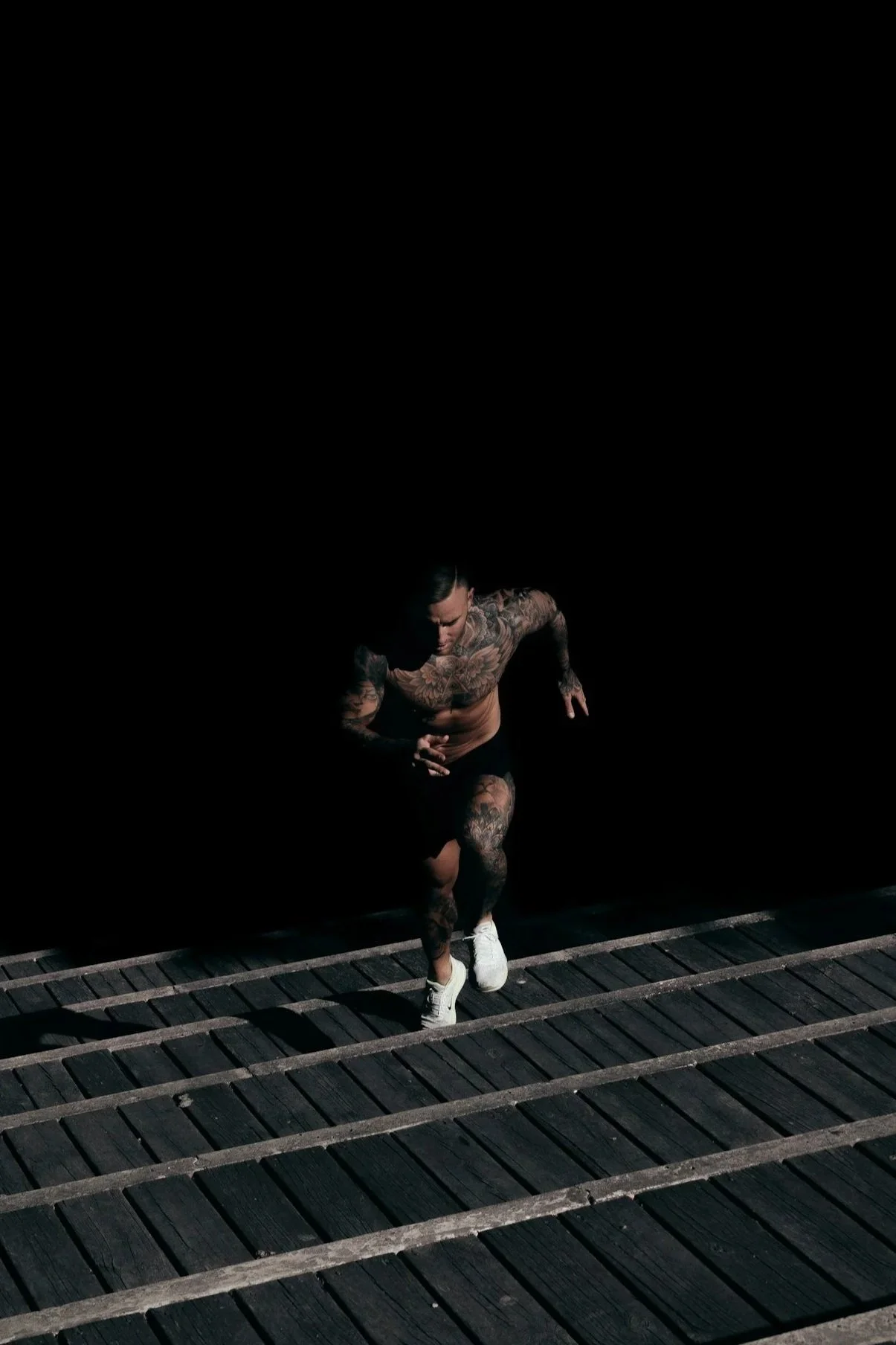 A tattooed man with a muscular build running on a dark outdoor track at night.