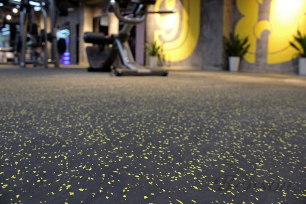 Gym interior with exercise equipment, yellow wall with designs, and a textured black and yellow speckled floor.