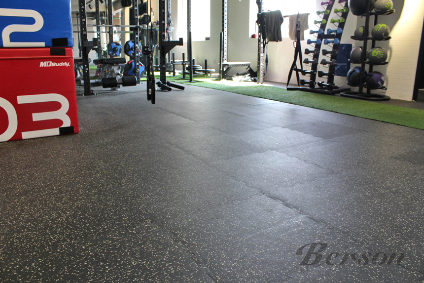 Interior of a gym with weightlifting equipment, medicine balls on a rack, and a section of artificial turf for exercises.