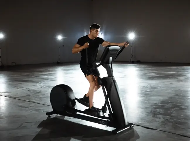 A man running on a treadmill in a dimly lit space with bright lights in the background.