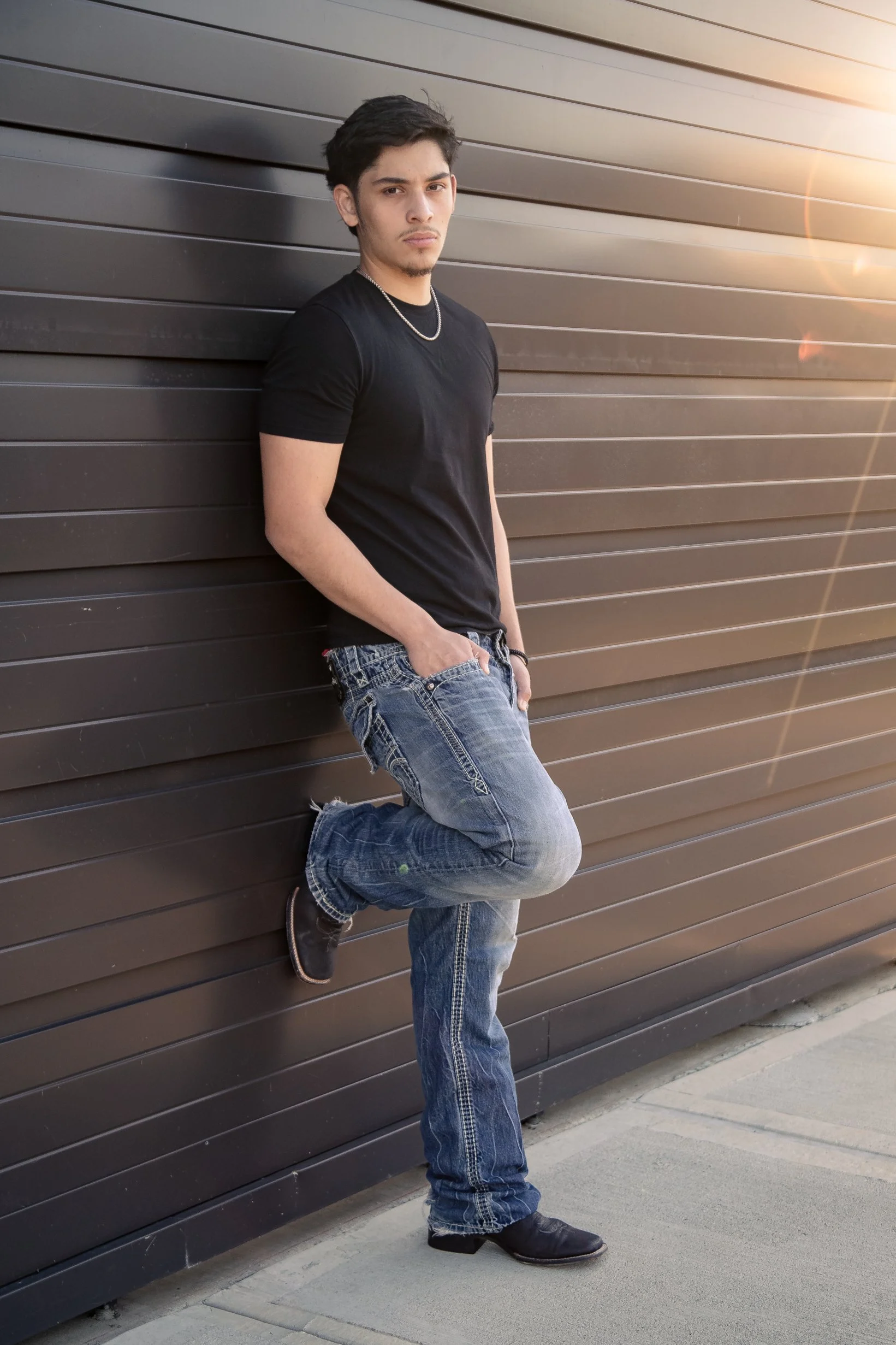 High school senior portrait featuring a male senior in a relaxed pose against a modern urban wall with warm sunset light. Contemporary senior photography by Dominic Alvarez Photography serving Houston, Katy, and surrounding areas across Southeast Tex