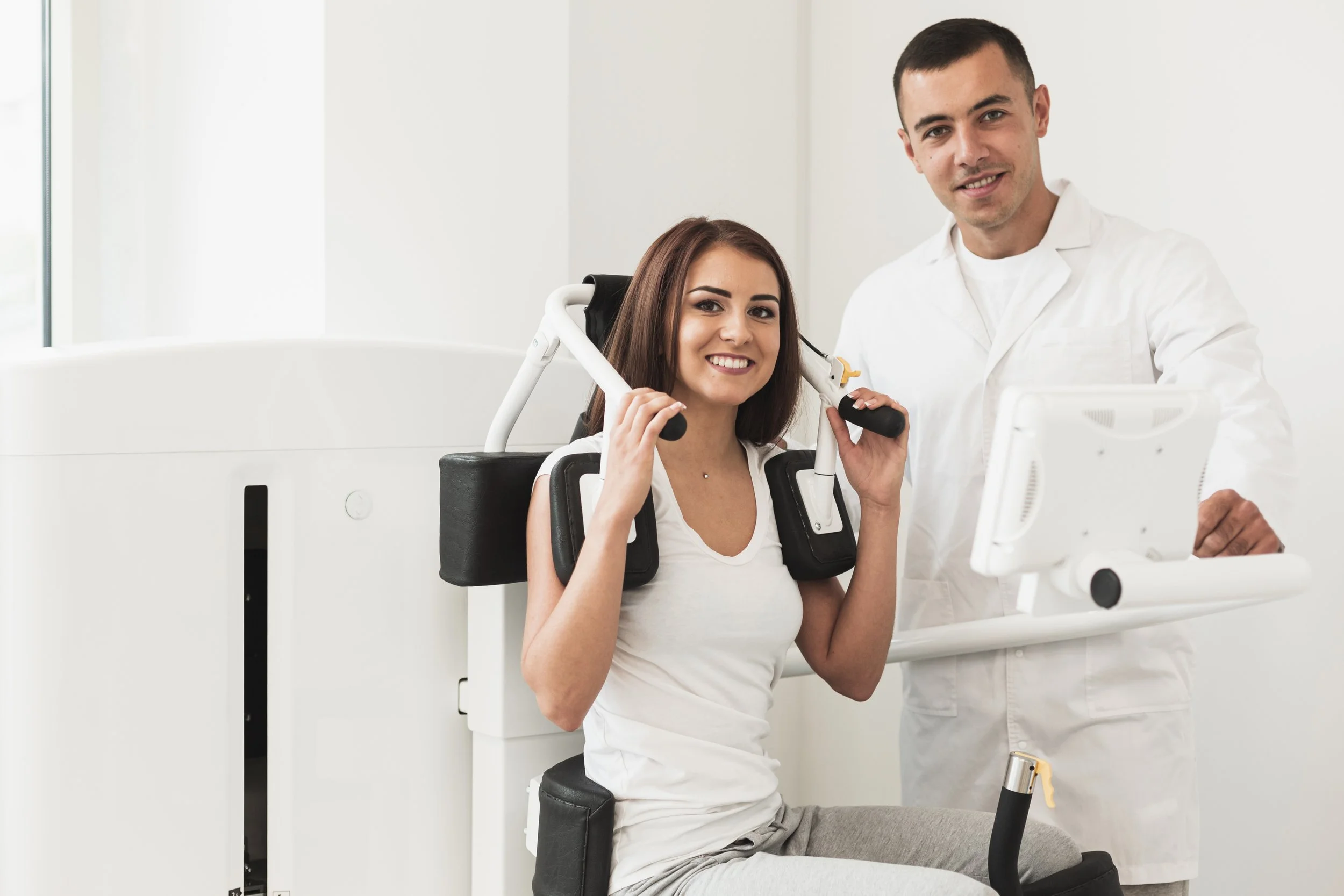 A woman using a rehabilitation device with a healthcare professional next to her, in a medical setting.
