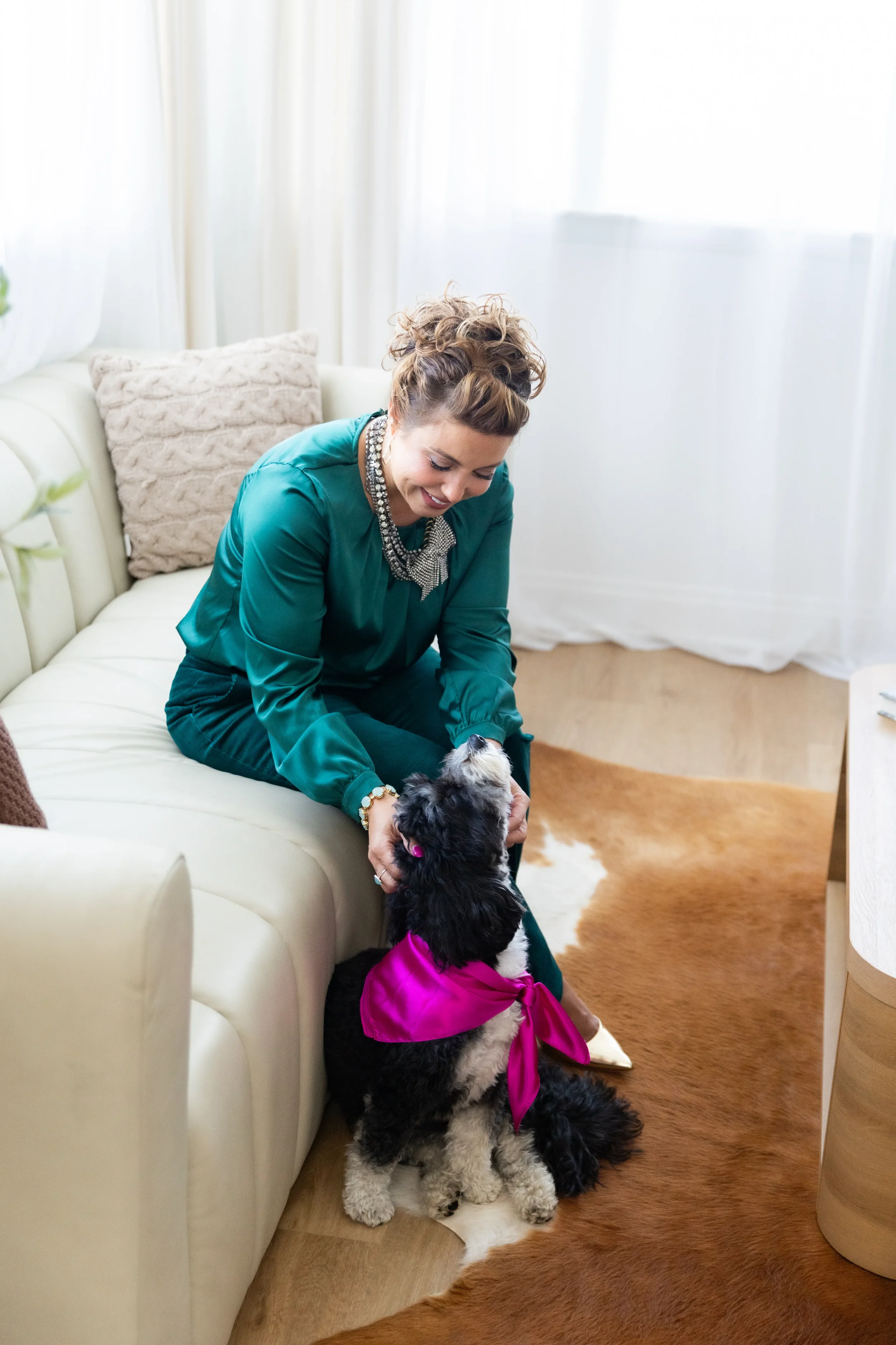Woman in green sweater playing with a black and white dog wearing a pink bandana in a living room.