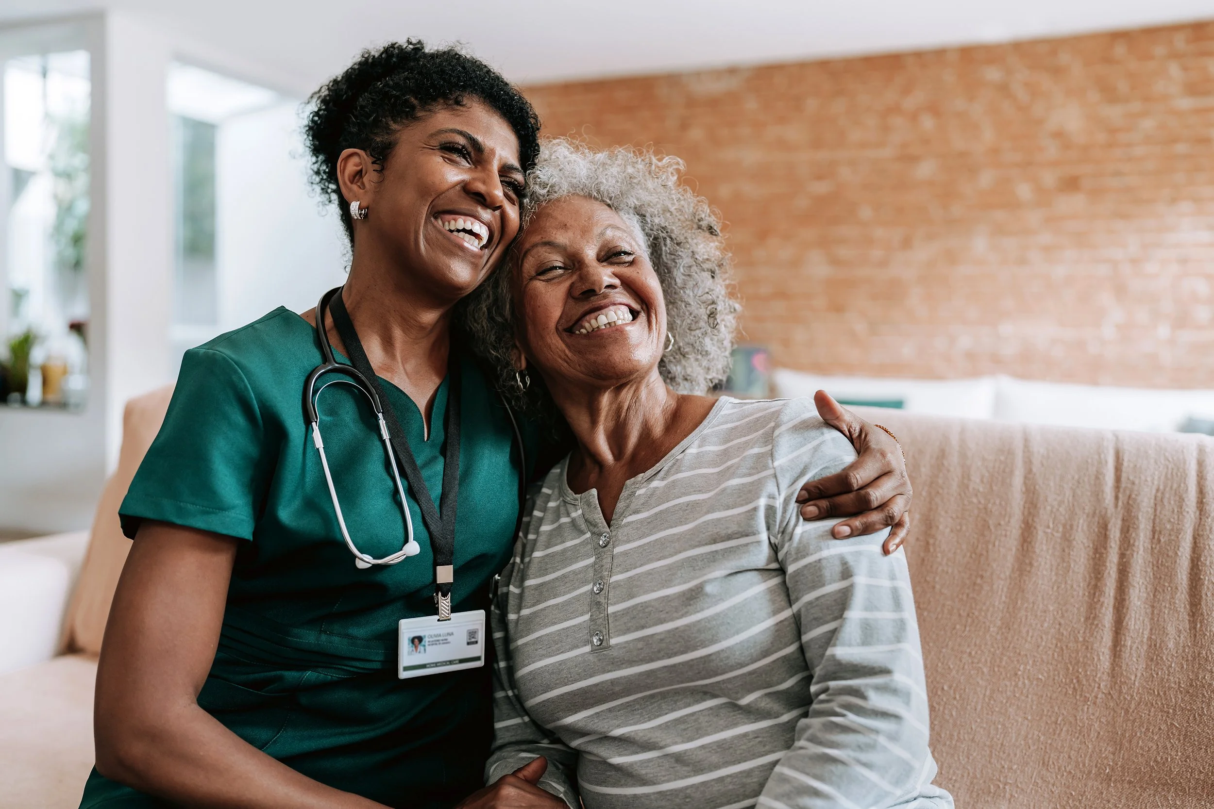Nurse hugging an elderly woman in a bright room.