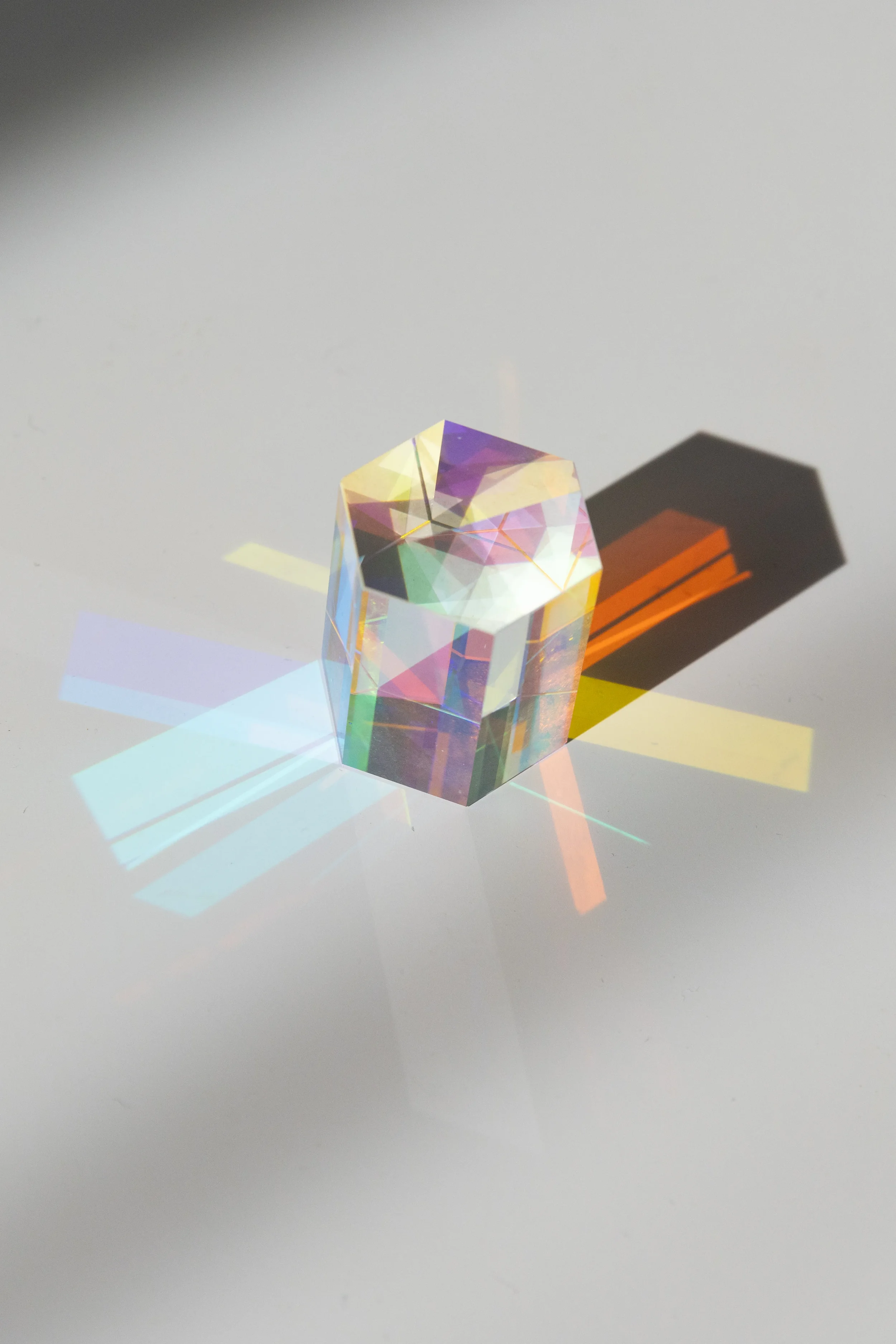 A prism with an iridescent surface creating colorful rainbow reflections and shadows on a white surface.
