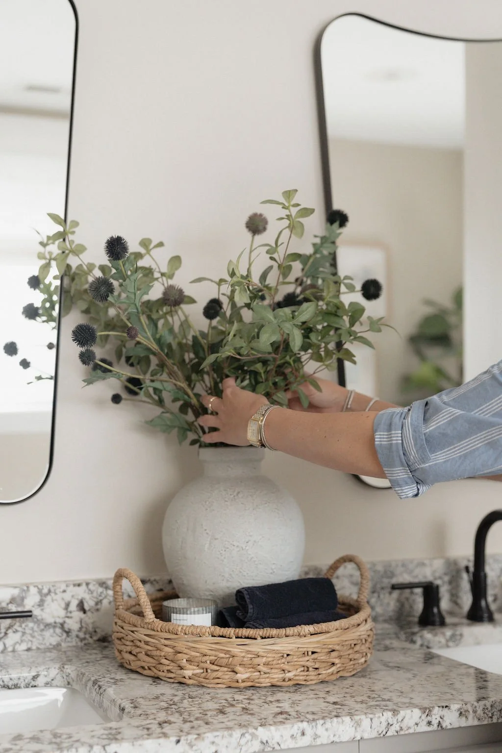 Person arranging dark purple flowers with green leaves in a white vase on a speckled granite countertop.