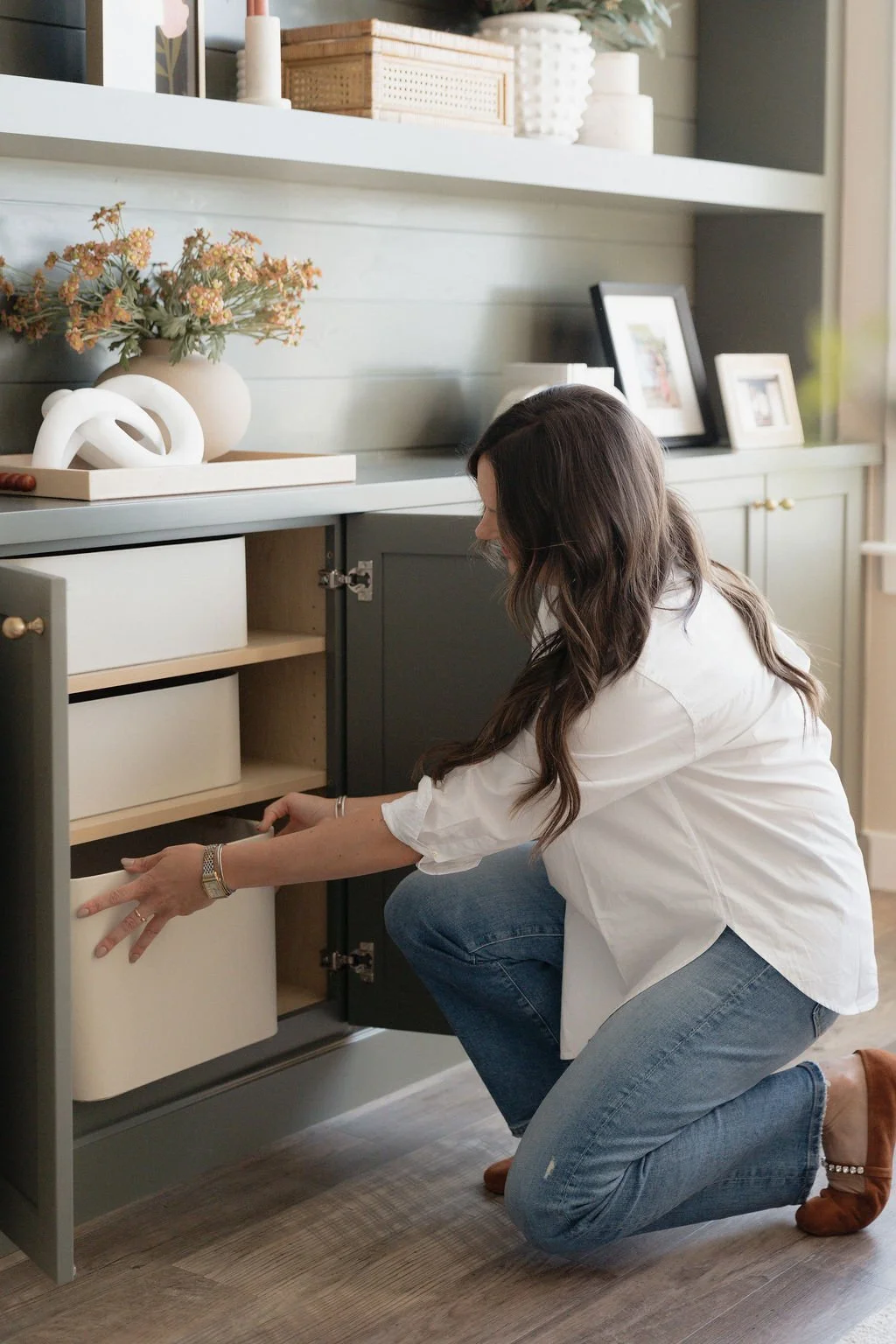 A woman kneeling in front of an open cabinet, organizing or retrieving items inside.
