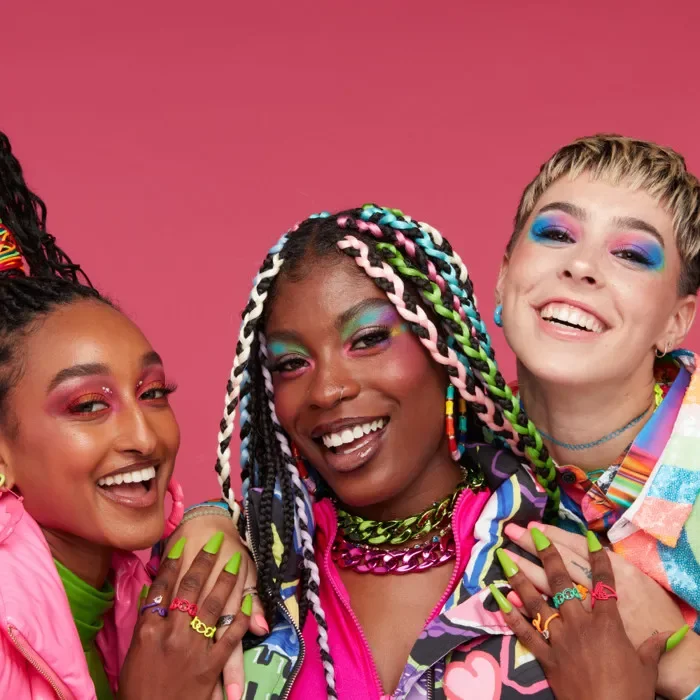 A middle-aged man with slicked-back gray hair sitting on a beige bench against a neutral wall, casting a shadow to his right, wearing a blue short-sleeved sweater and beige pants.