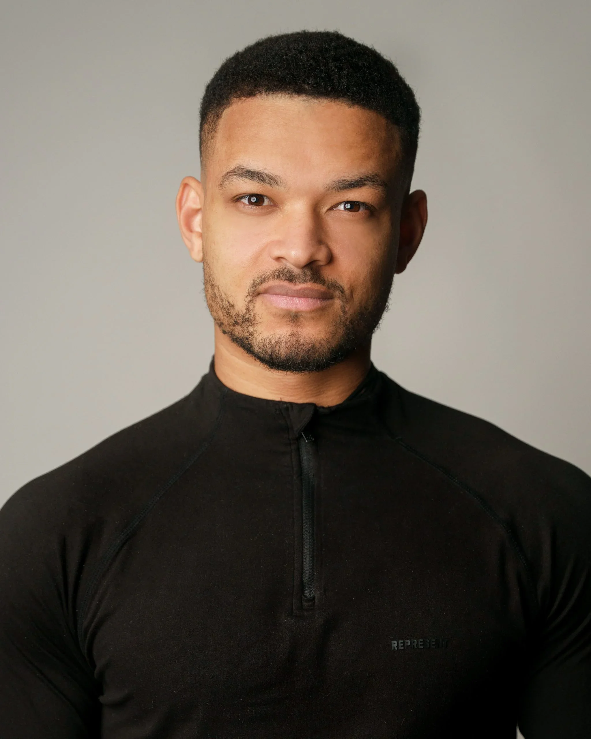 A woman with shoulder-length dark hair sitting on a white bench against a wooden wall, writing in a notebook. Next to her, there is a framed abstract art piece leaning against the wall.