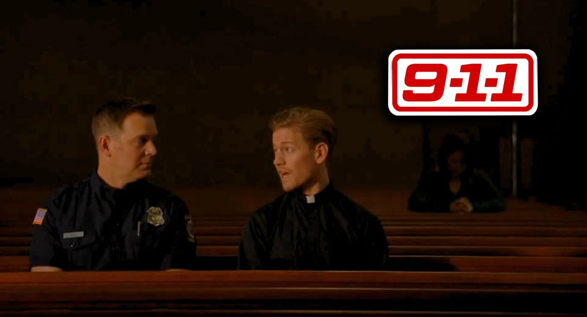 A scene from the movie 'Dogma' with two men in church pews, one dressed as a police officer and the other as a priest, looking at each other, and a woman sitting in the background. There's a '9-1-1' logo in the top right corner.