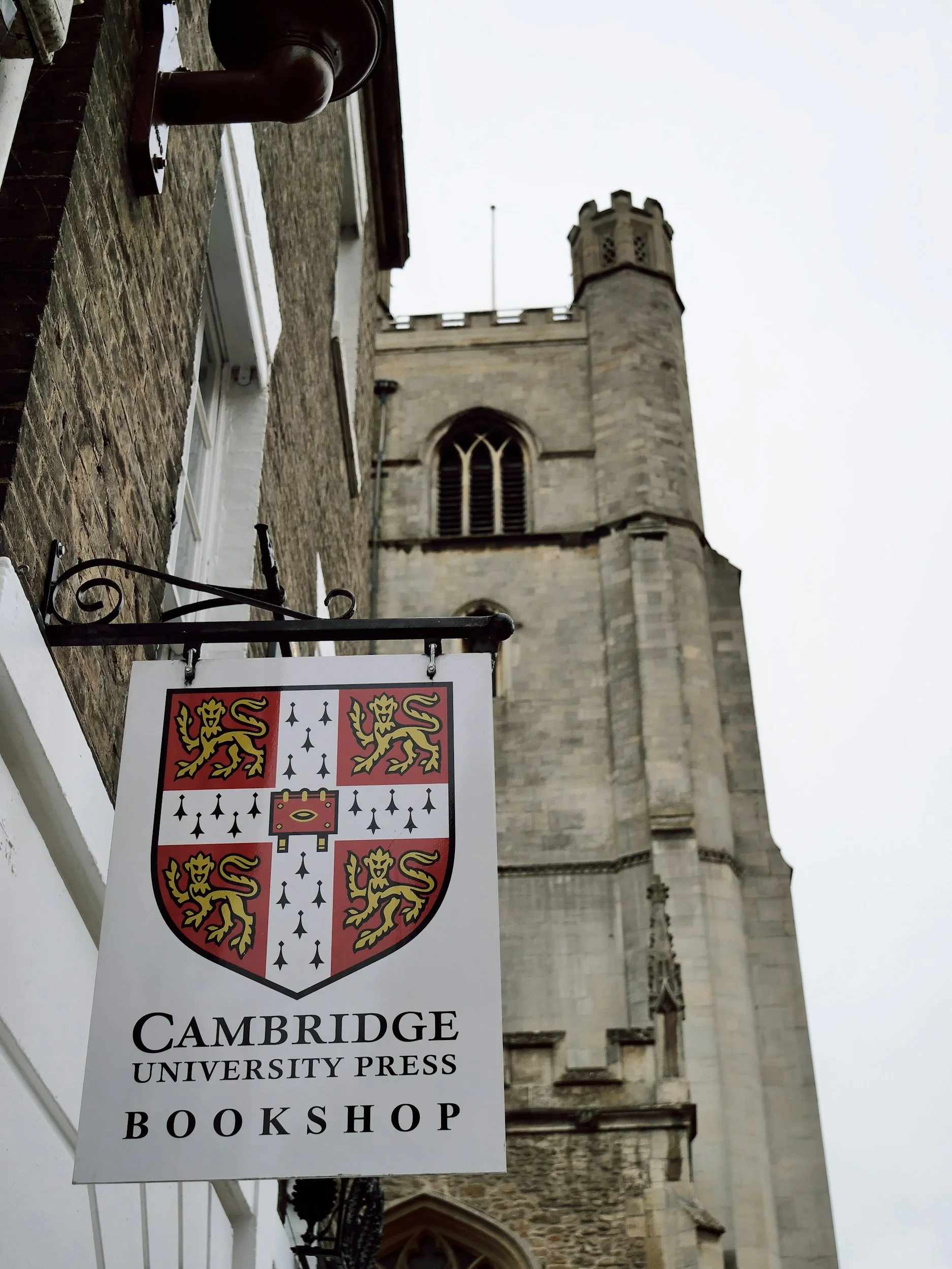 Sign for Cambridge University Press Bookshop in front of a historic stone church or cathedral tower.
