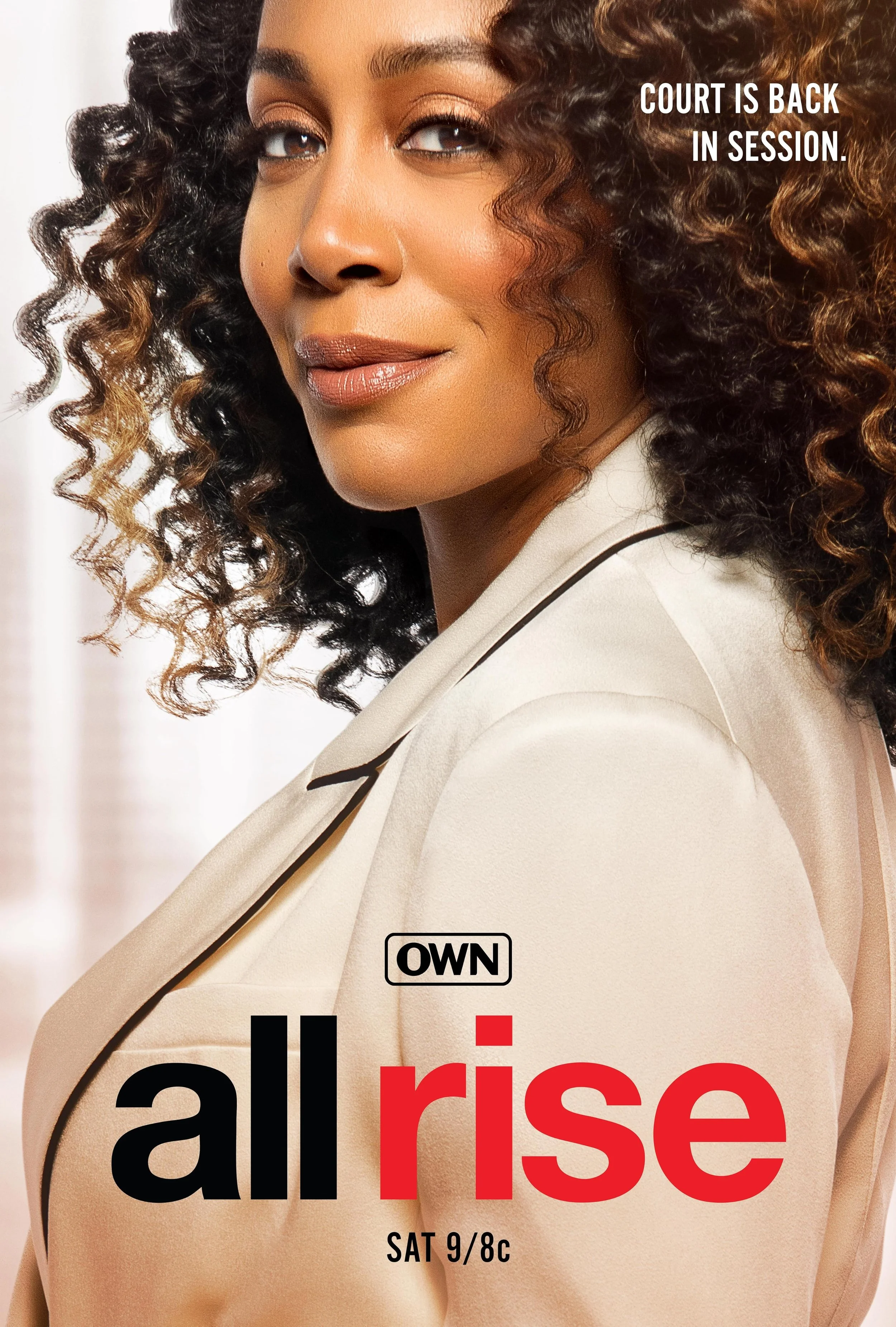 Close-up portrait of a confident woman with curly hair, wearing a beige blazer, looking at the camera. Text on the image reads 'Court is back in session.' and 'OWN all rise,' with a TV show schedule 'SAT 9/8c.'