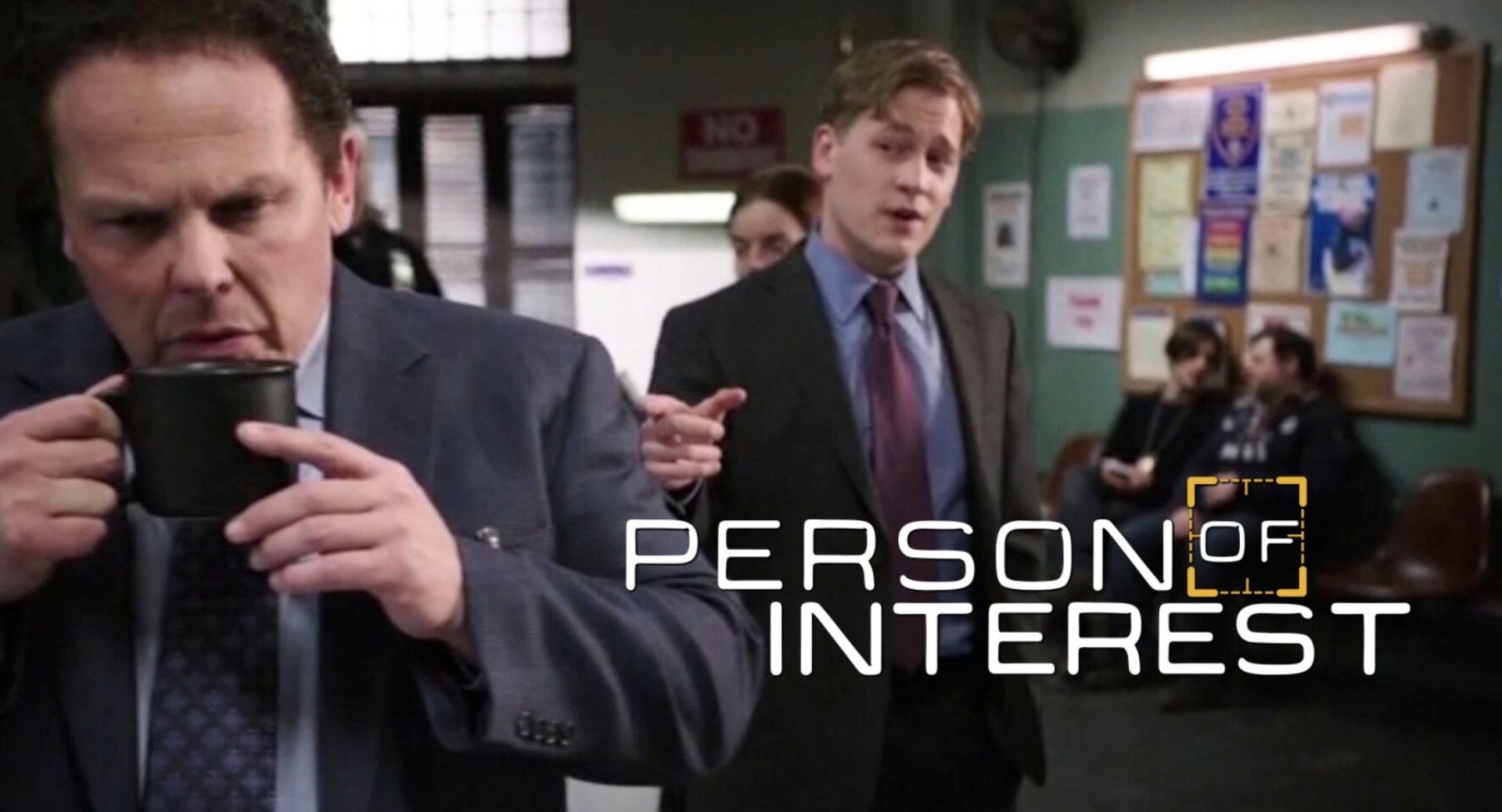 Scene from the TV show 'Person of Interest' featuring men in suits inside a police station or office, with one man in the foreground holding a coffee mug and another pointing towards him.