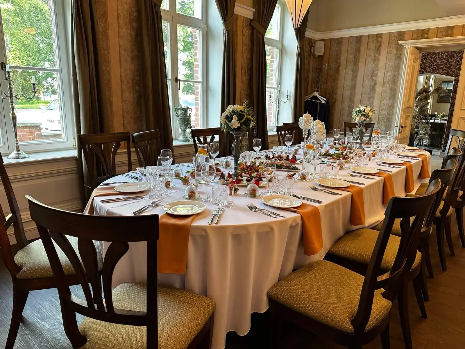 Šventinis apvalaus stalo serviravimas su žvakėmis ir oranžinėmis detalėmis Klaipėdoje.