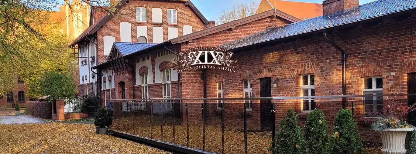 Raudonų plytų istorinis restorano „XIX amžius“ pastatas Klaipėdoje rudens fone.