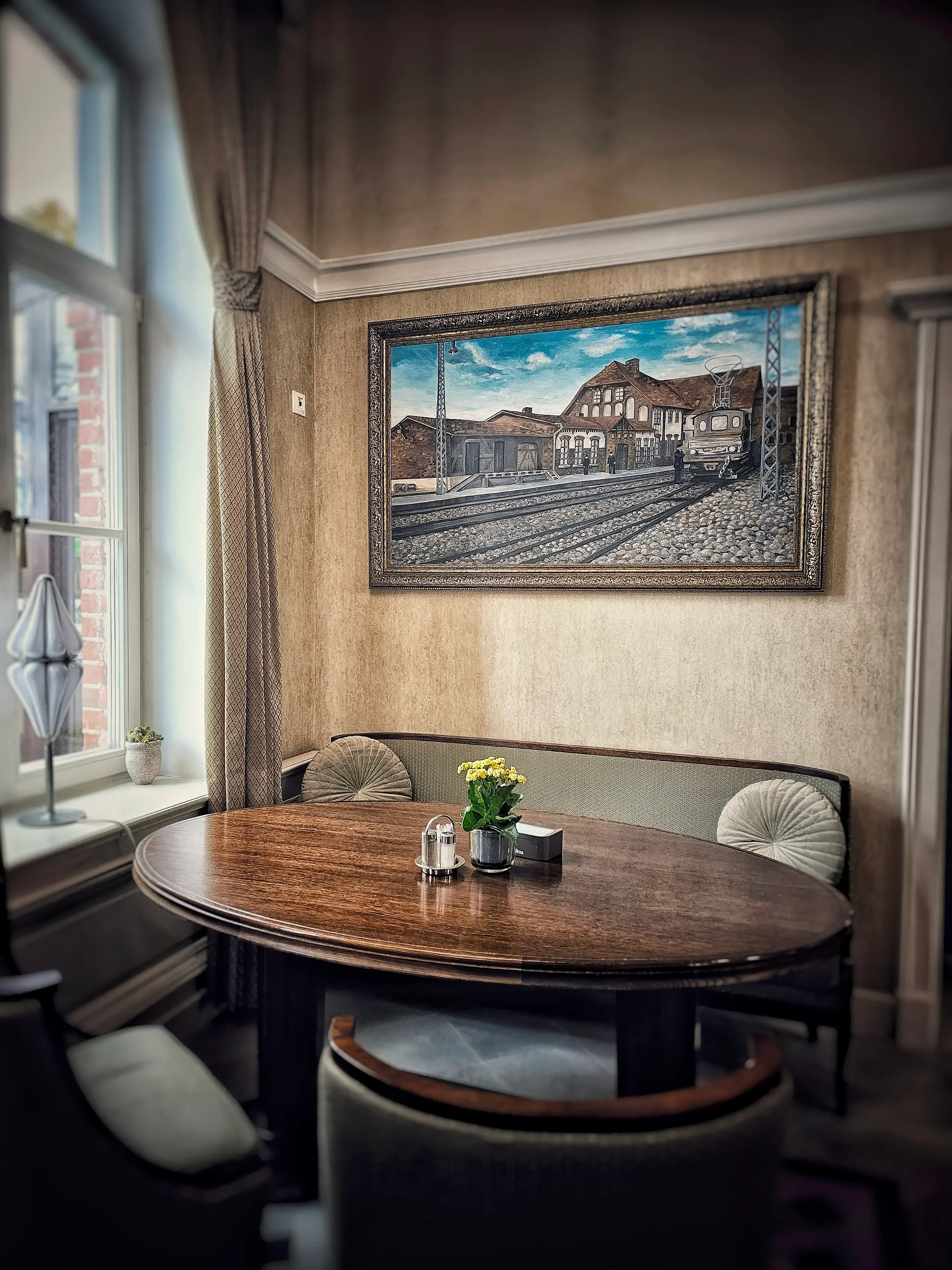 Restorano erdvė su minkštasuoliu ir istoriniu paveikslu, vaizduojančiu traukinių stotį.