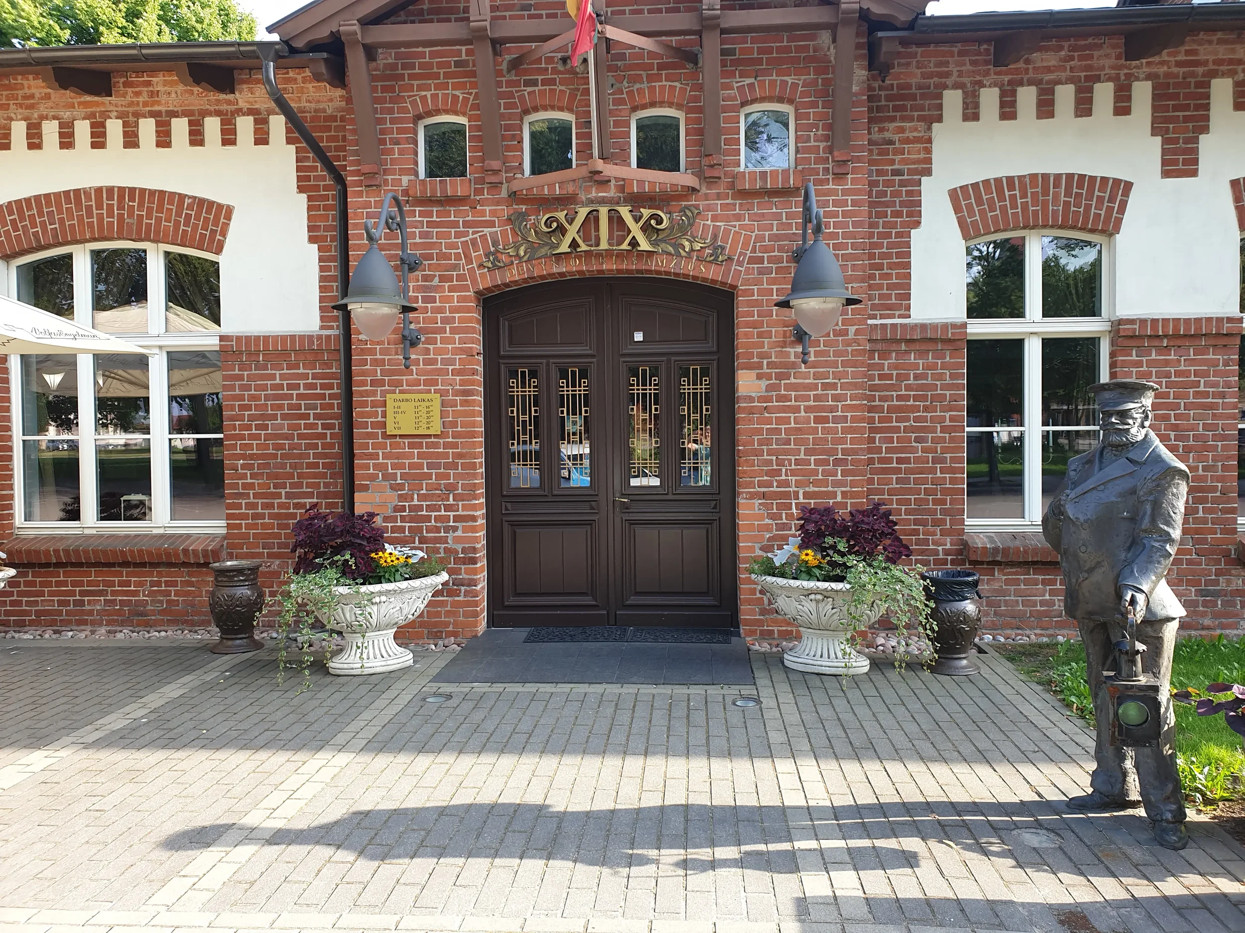 Restorano „XIX amžius“ pagrindinis įėjimas su gėlėmis ir bronzine skulptūra Klaipėdoje.