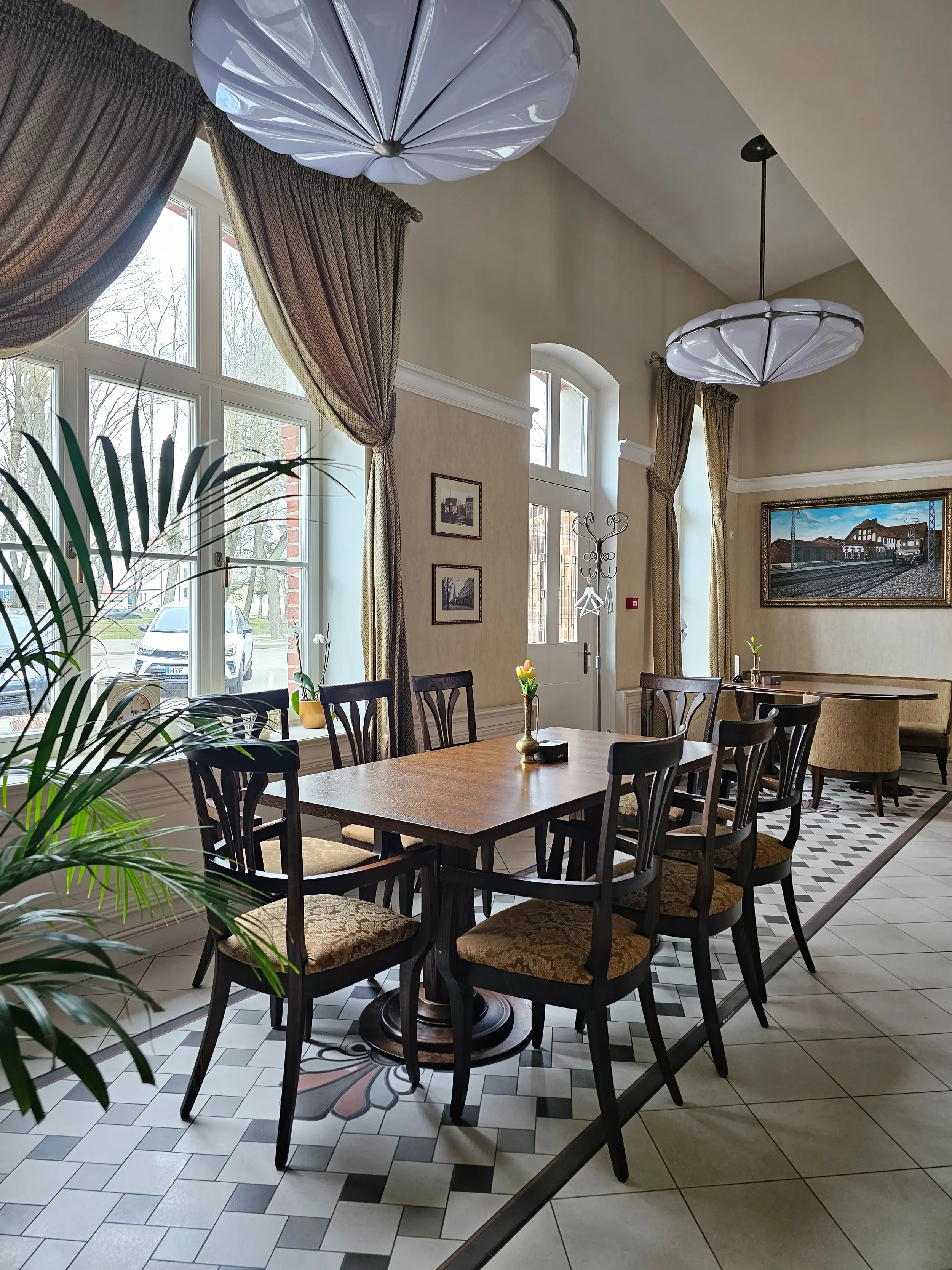 Šviesi ir jauki restorano erdvė Klaipėdoje su dideliais langais ir istoriniais paveikslais.