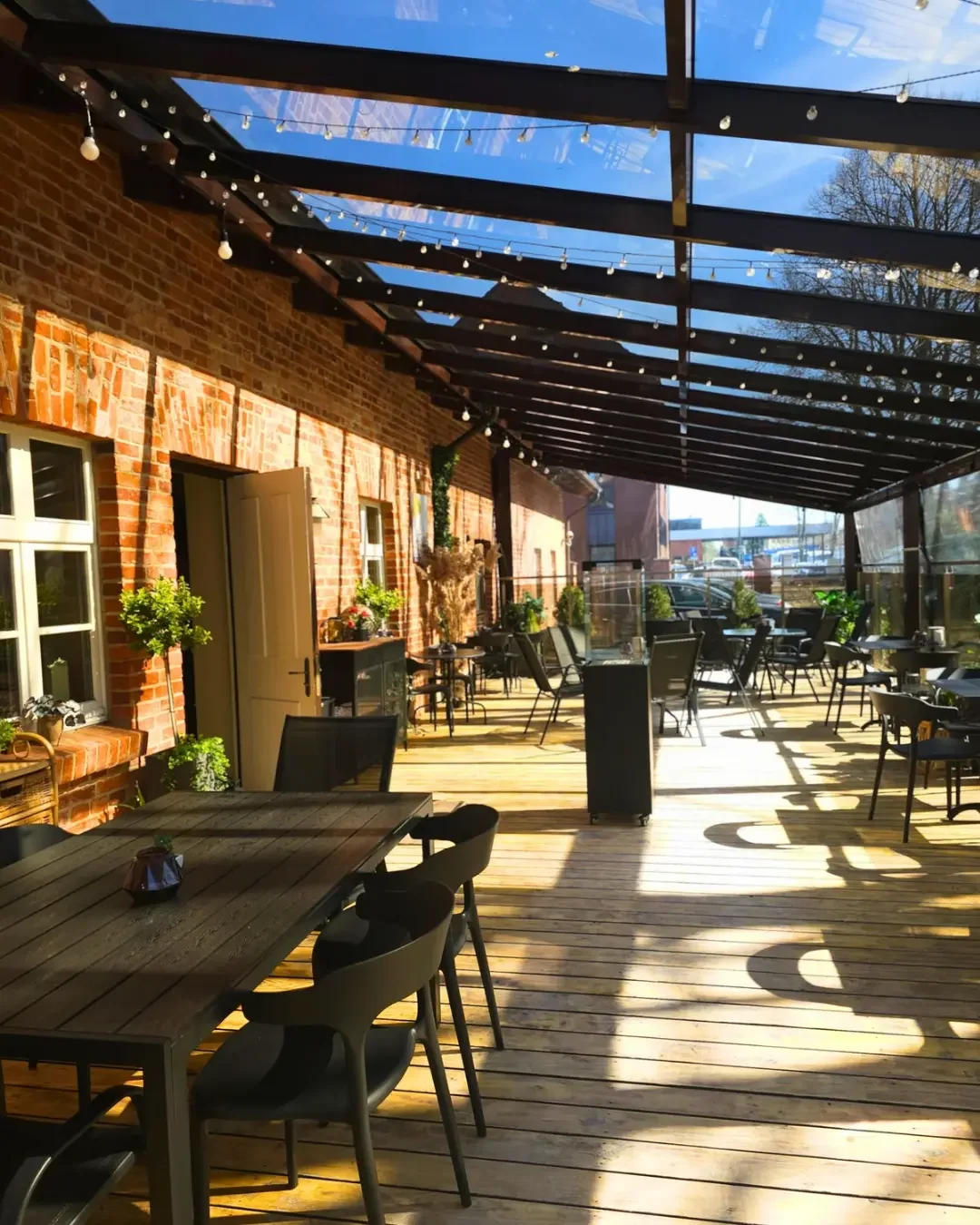 Lauko terasa su medinėmis grindimis, plytų sienomis ir romantišku lempučių apšvietimu.