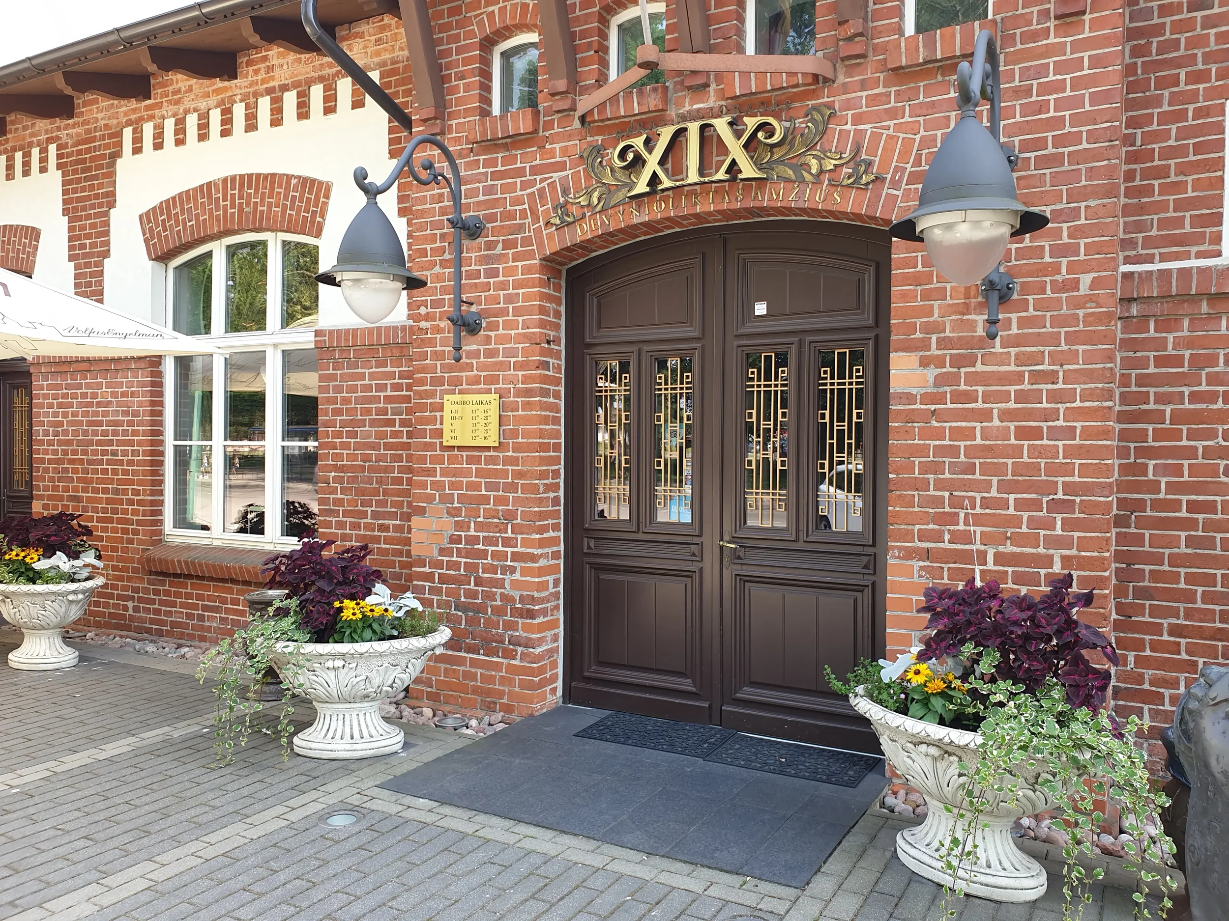 Pagrindinis įėjimas į istorinį restoraną „XIX amžius“ Klaipėdoje su puošniomis gėlėmis.