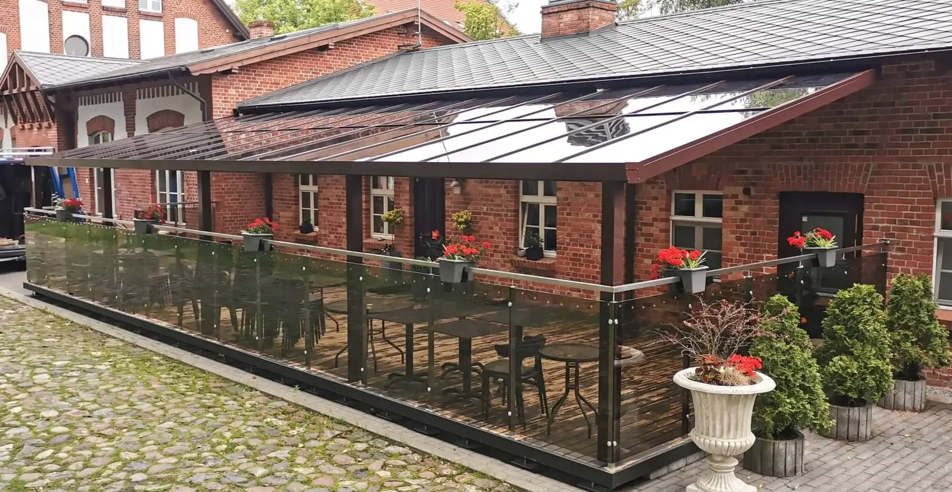 Jauki lauko terasa su stiklinėmis sienomis ir vaizdu į istorinį pastatą Klaipėdoje.