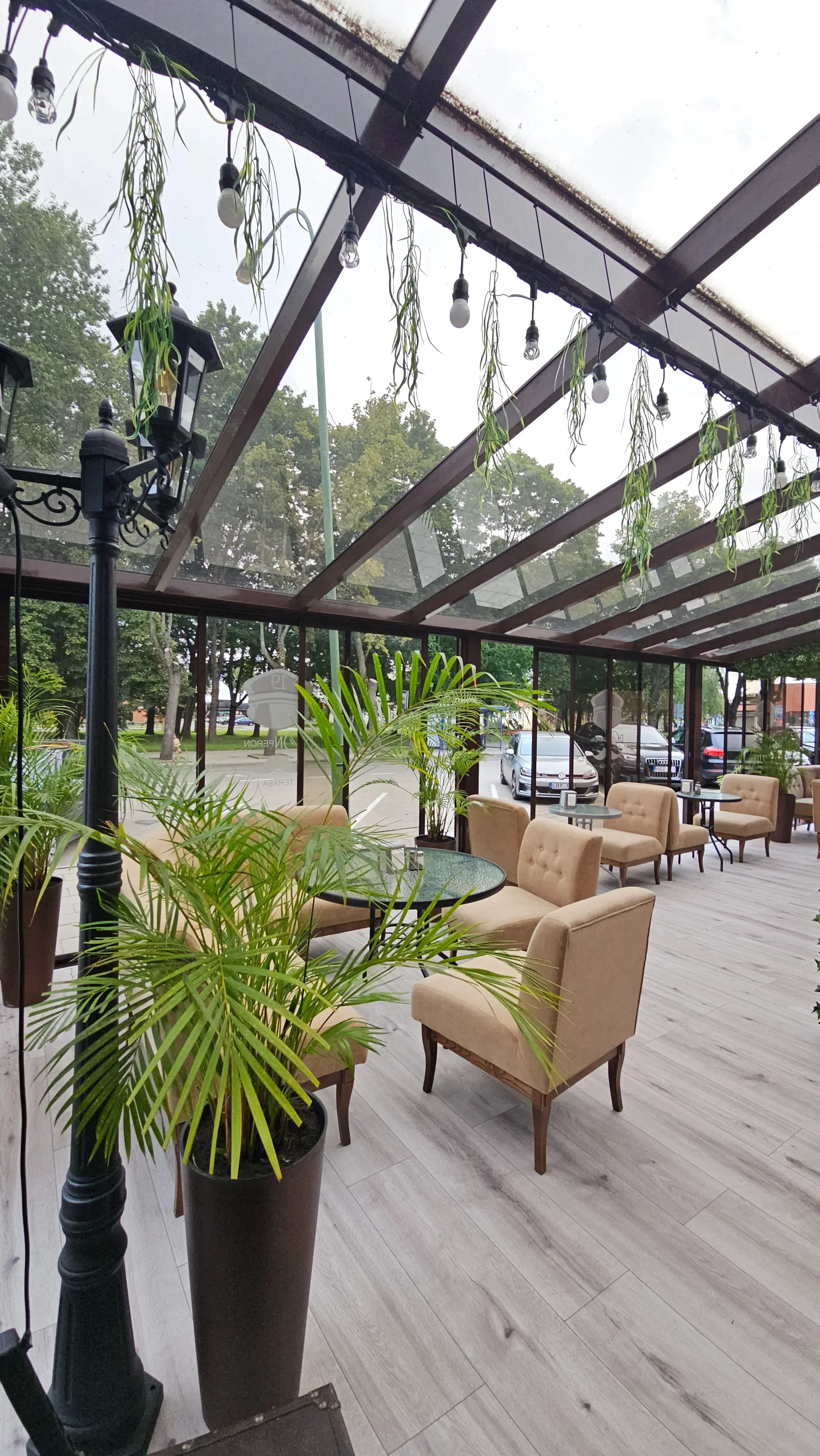 Šviesi restorano „XIX amžius“ erdvė su minkštais krėslais, augalais ir natūralia šviesa.