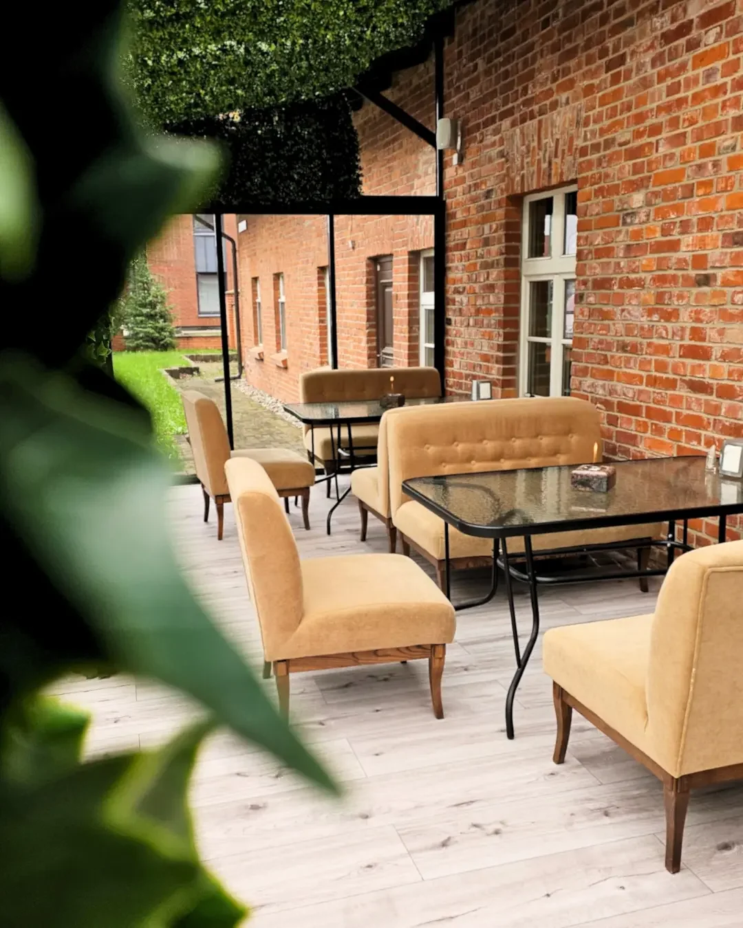 Jauki ir šviesi įstiklinta restorano lauko terasa su minkštais krėslais.