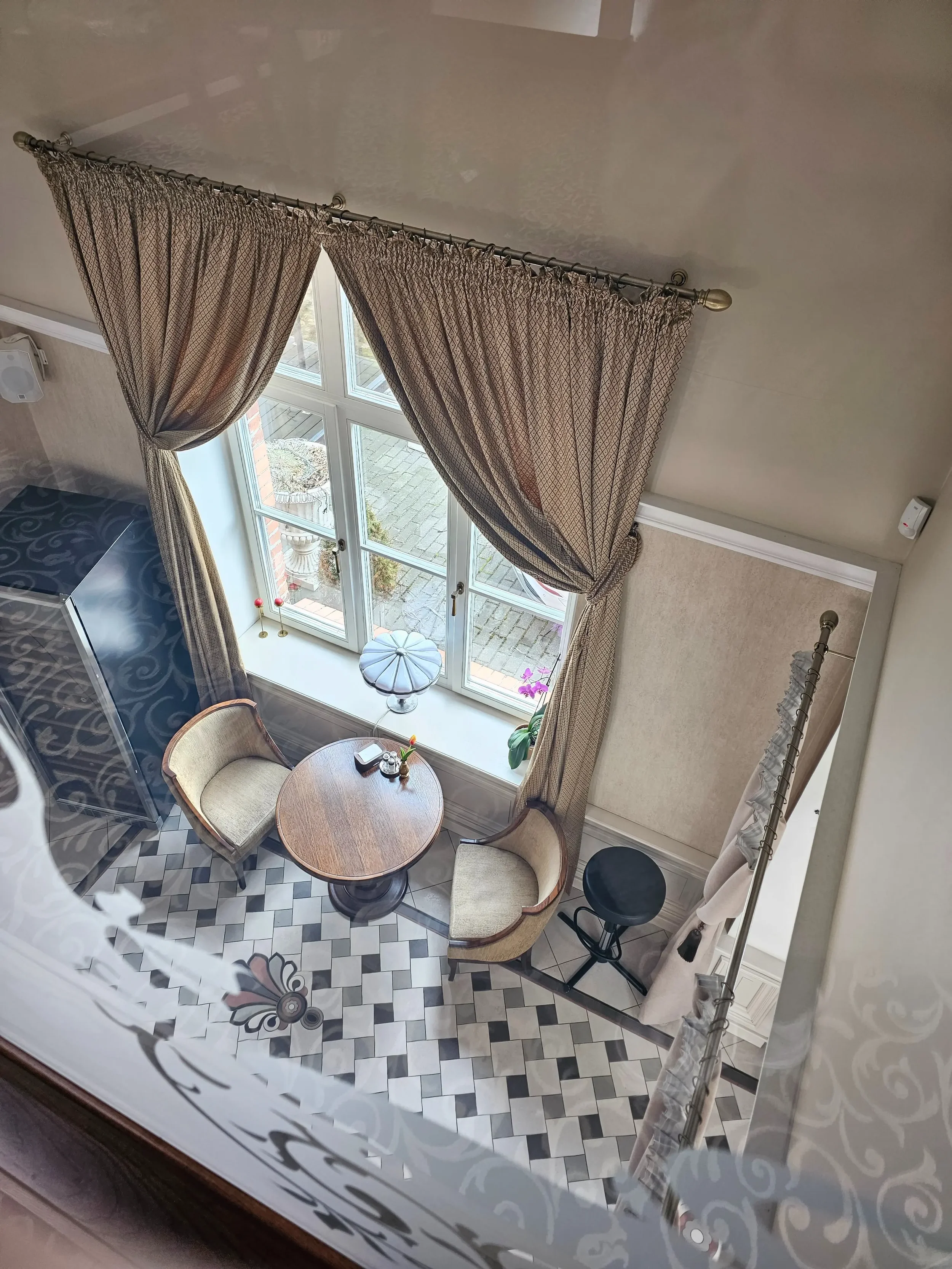 Restorano „XIX amžius“ interjero detalės: apvalus stalas ir minkšti krėslai prie lango.