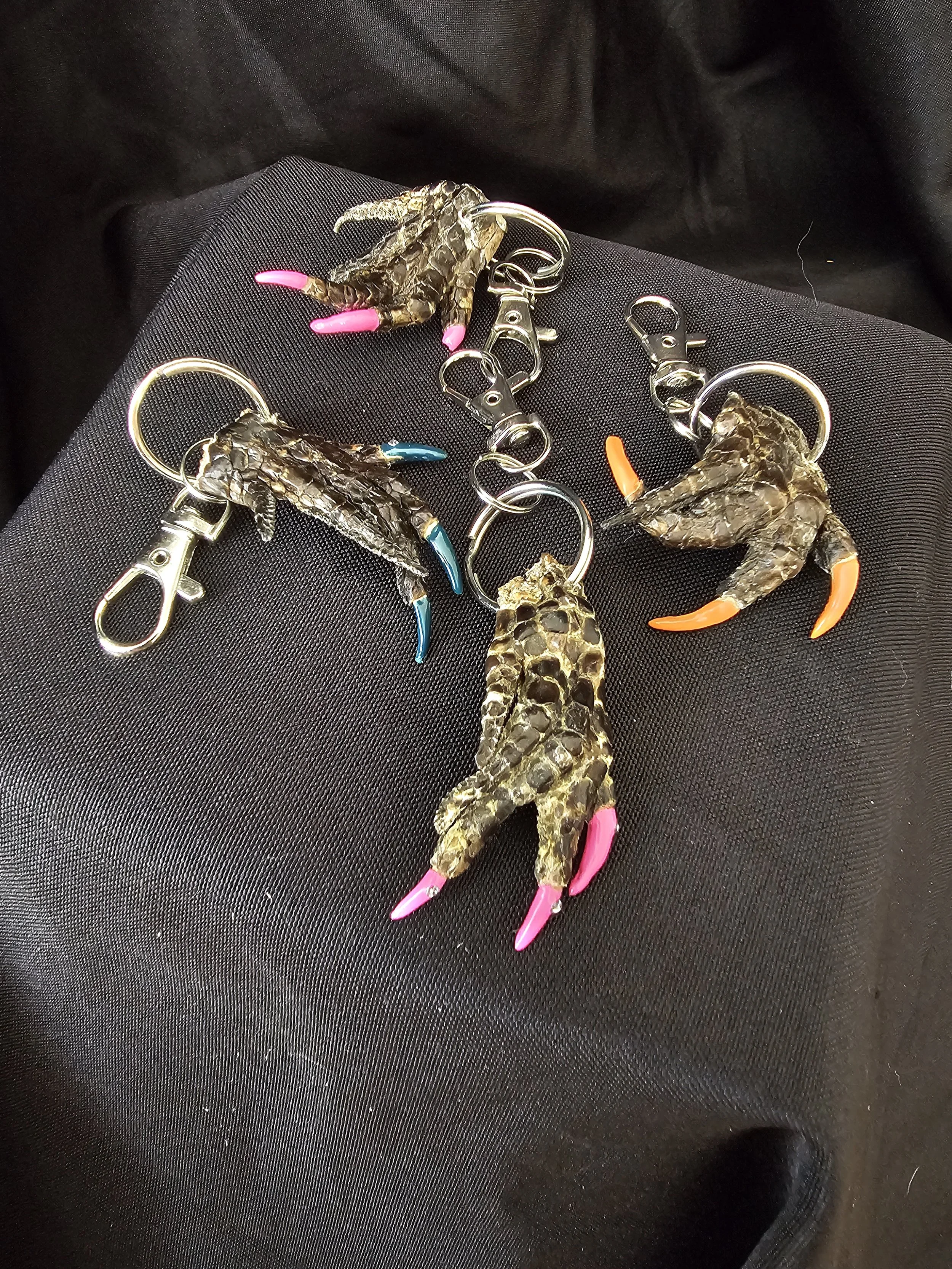 Set of keychains with claws and textured dark brown surface, some nails painted pink, blue, and orange.