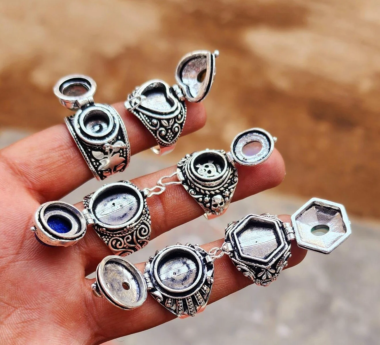 Hand holding several ornate silver rings and bracelet with various designs, some featuring empty or swirl-shaped settings and decorative patterns.