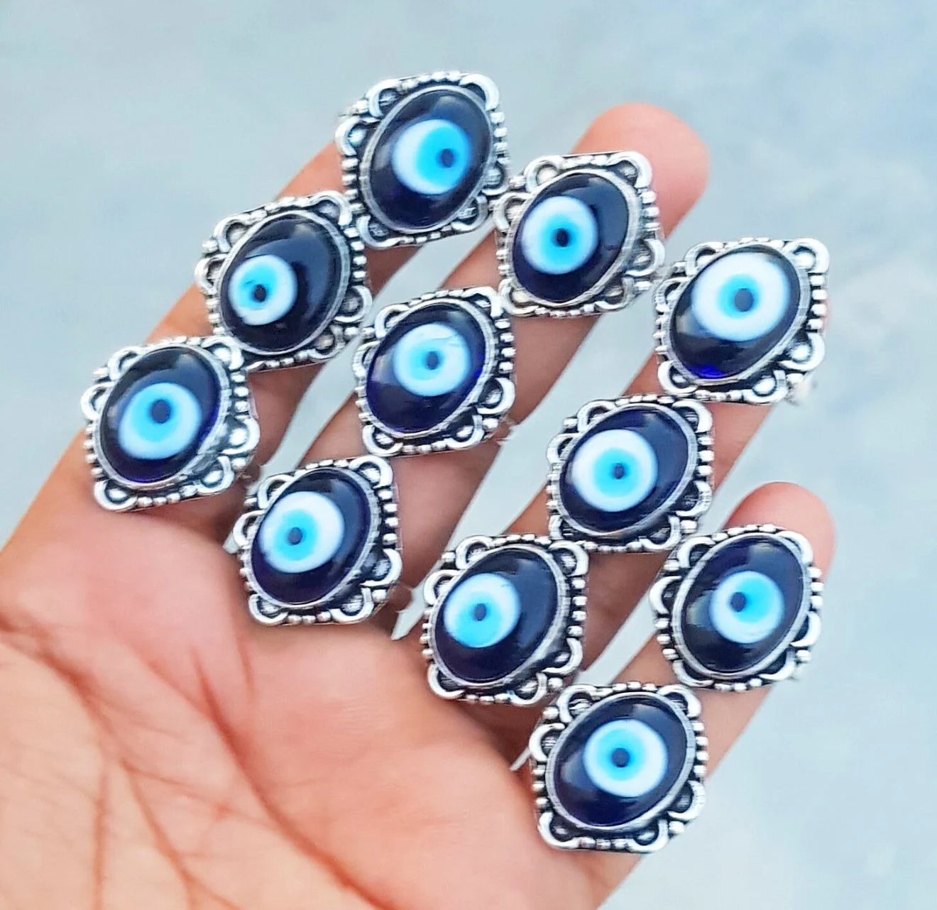 Multiple silver rings with blue eye designs held in a person's hand.